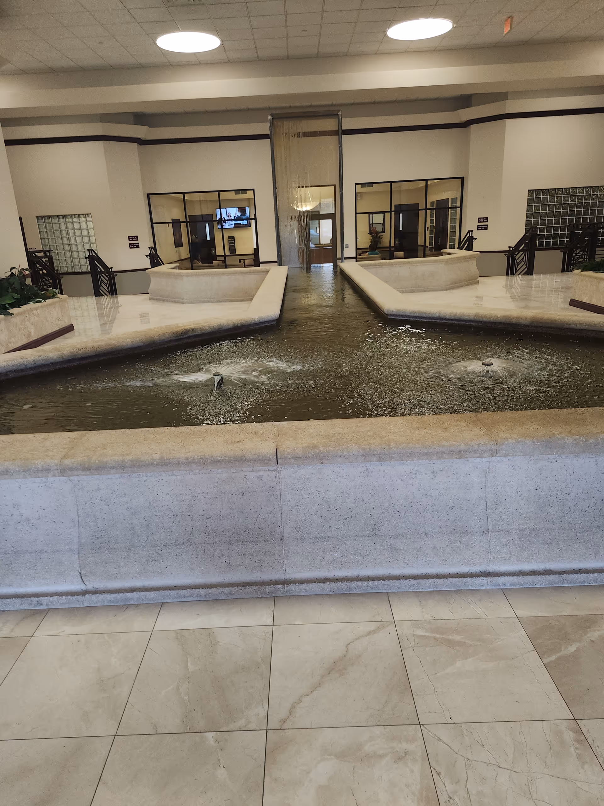 Interior lobby with a central water fountain and tiled marble floor.