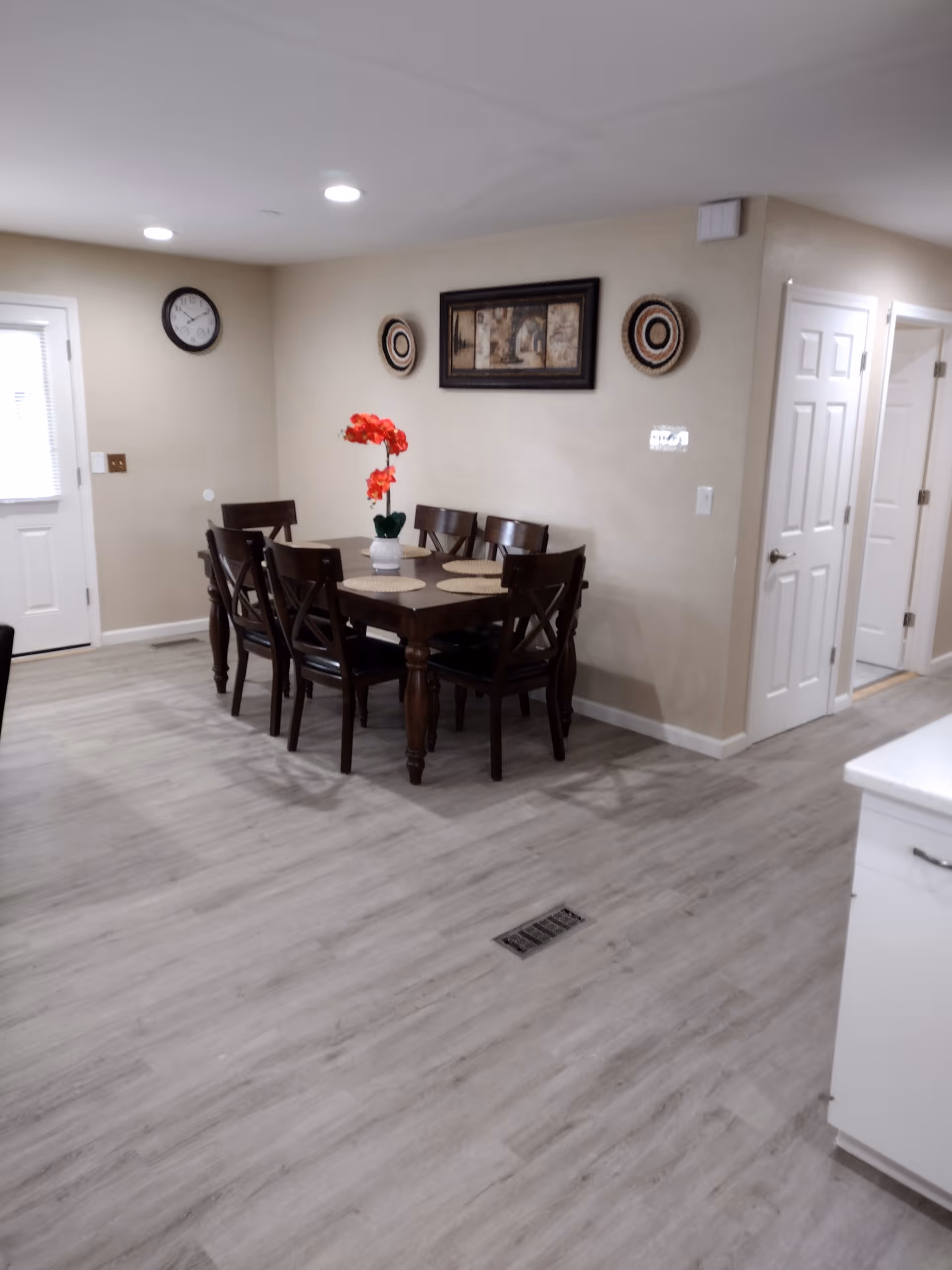 A dining room with a wooden table, six chairs, red flowers, and wall art.