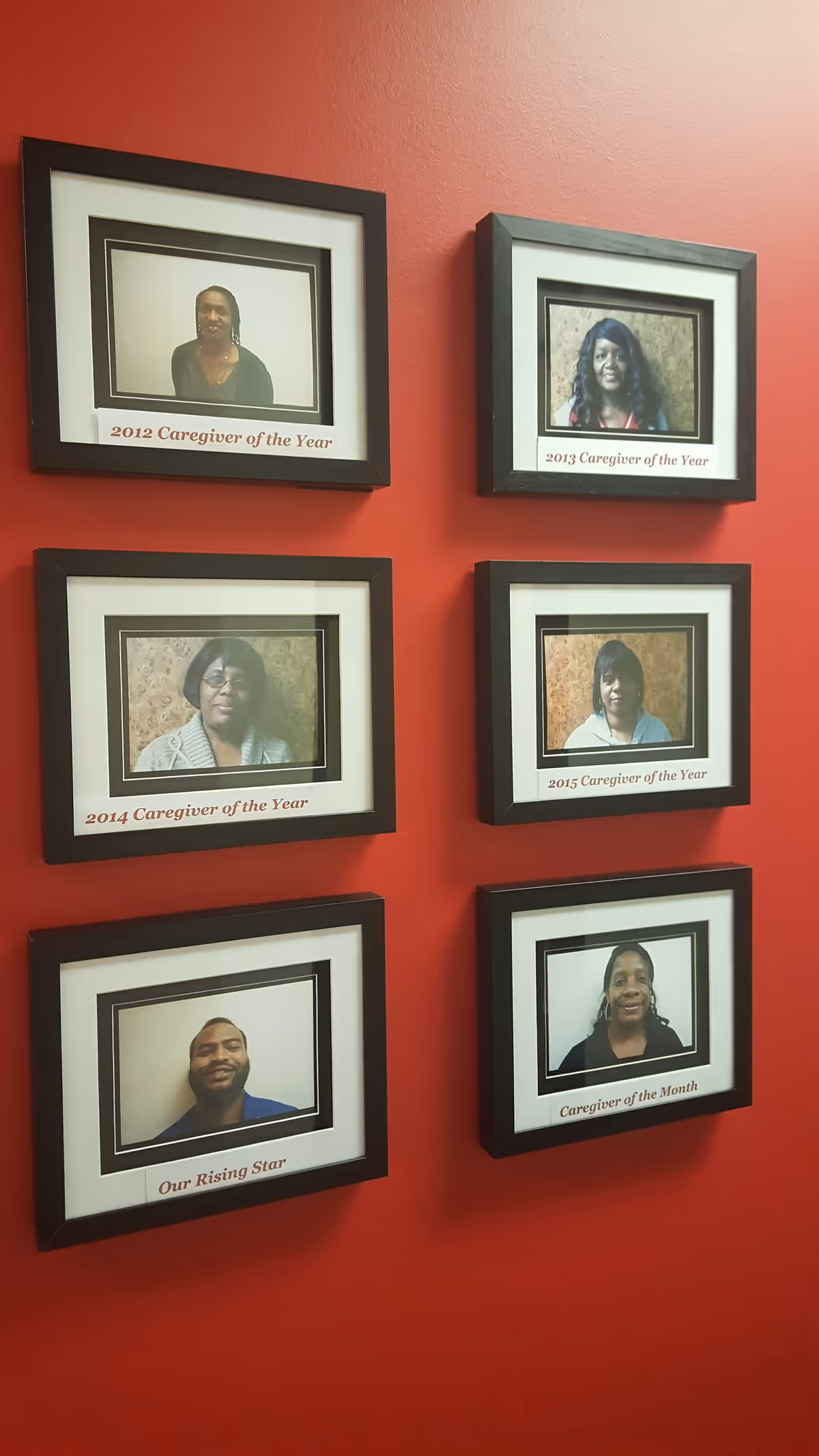 Red wall featuring six framed caregiver portraits with award captions.