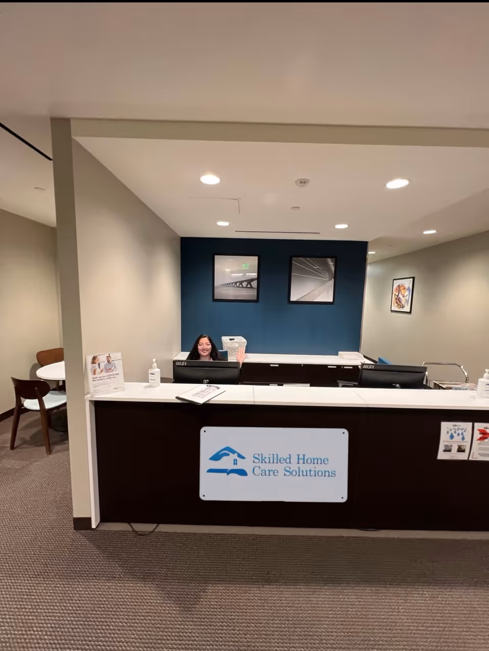 Reception desk with a smiling staff member waving in a modern senior care lobby.