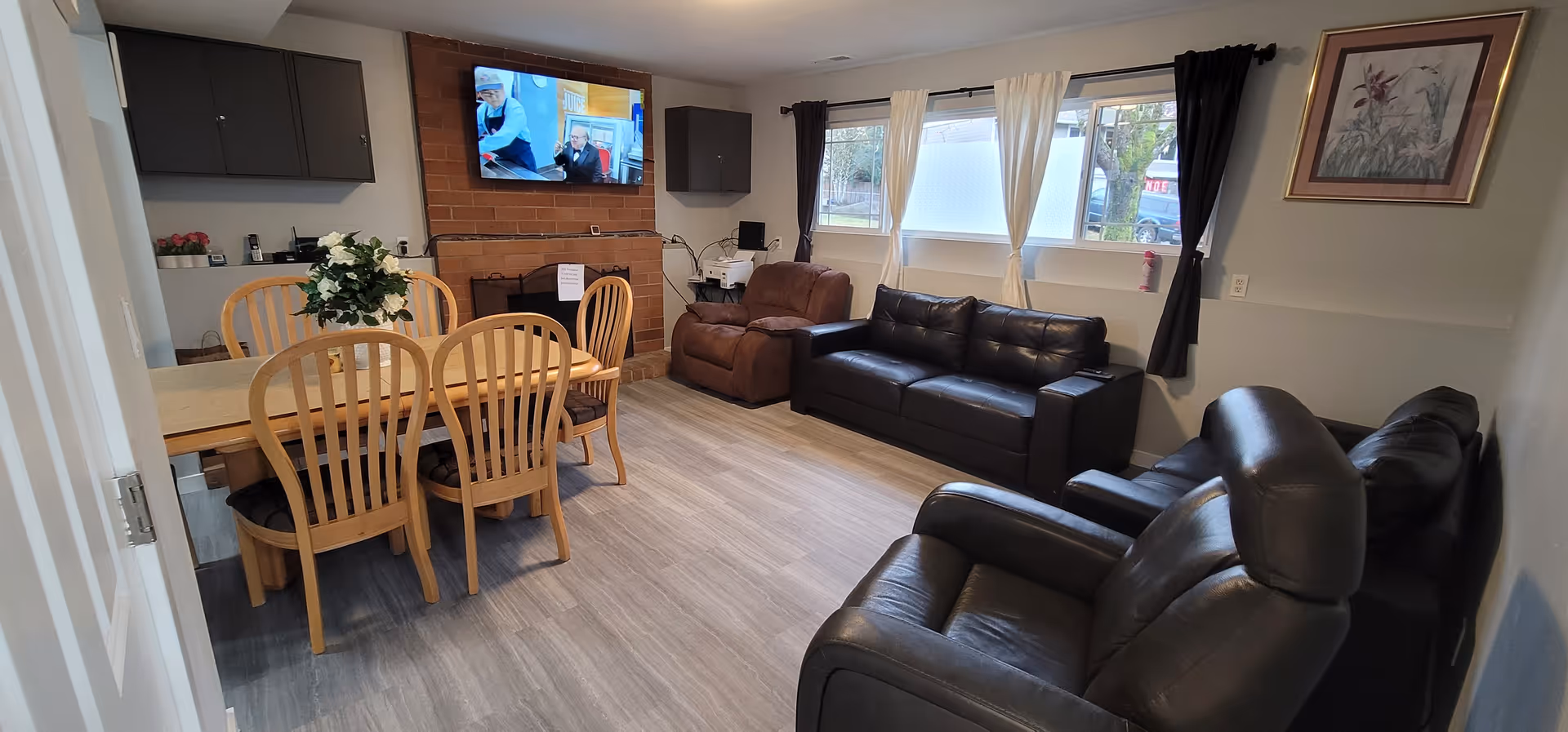 Cozy senior living common room with leather sofas, dining table, and wall-mounted TV.