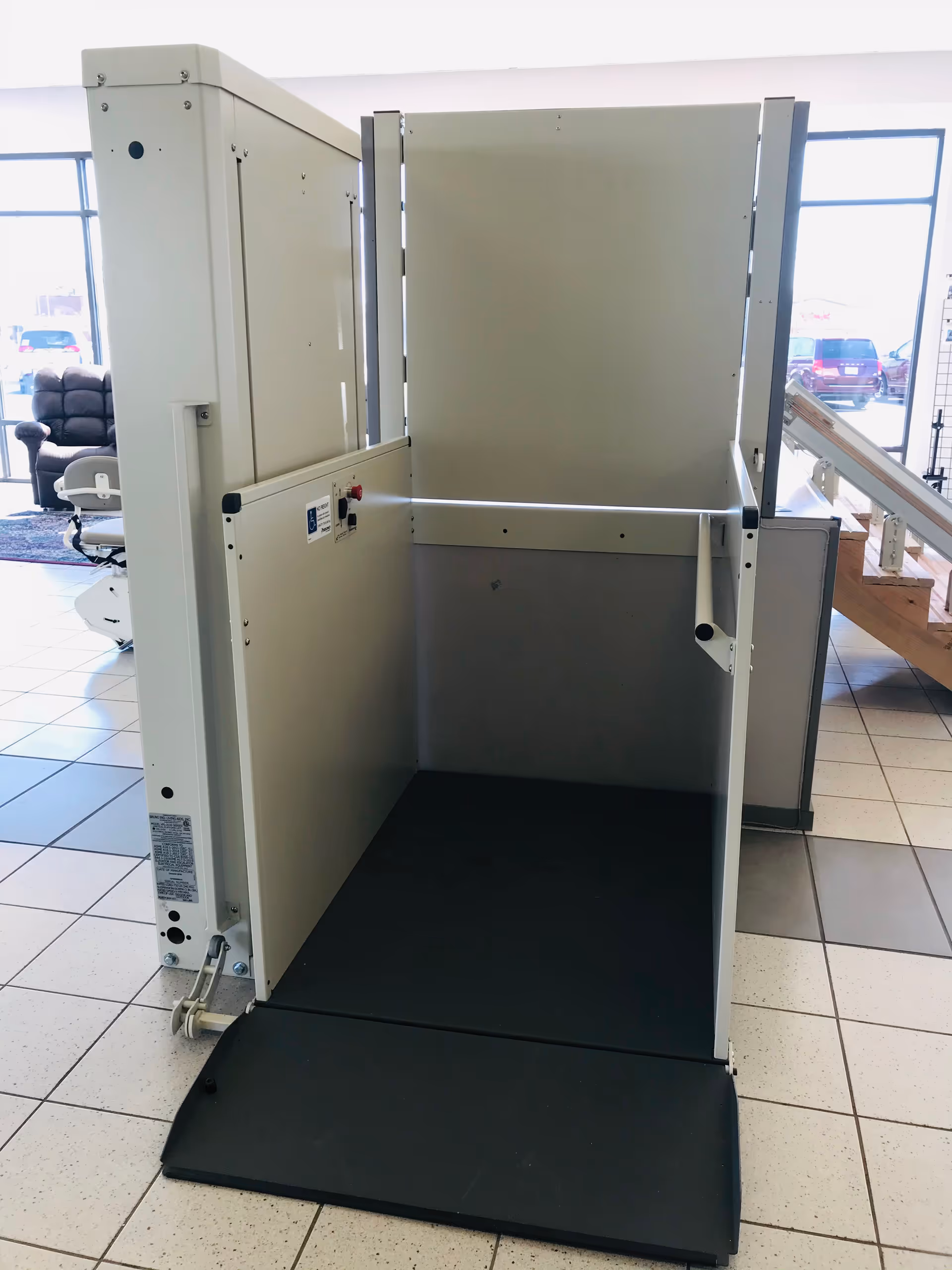 Indoor showroom area with a vertical patient lift apparatus and seating in background.