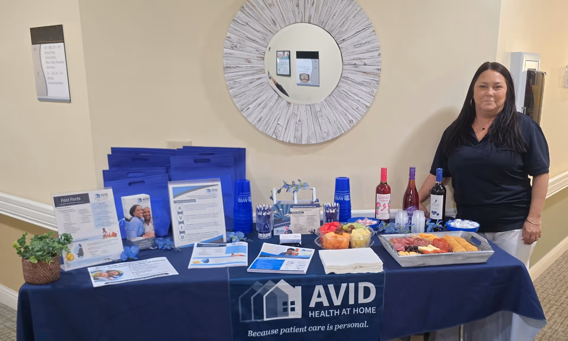 Promotional table with AVID Health at Home materials in a hallway, staff member standing beside.