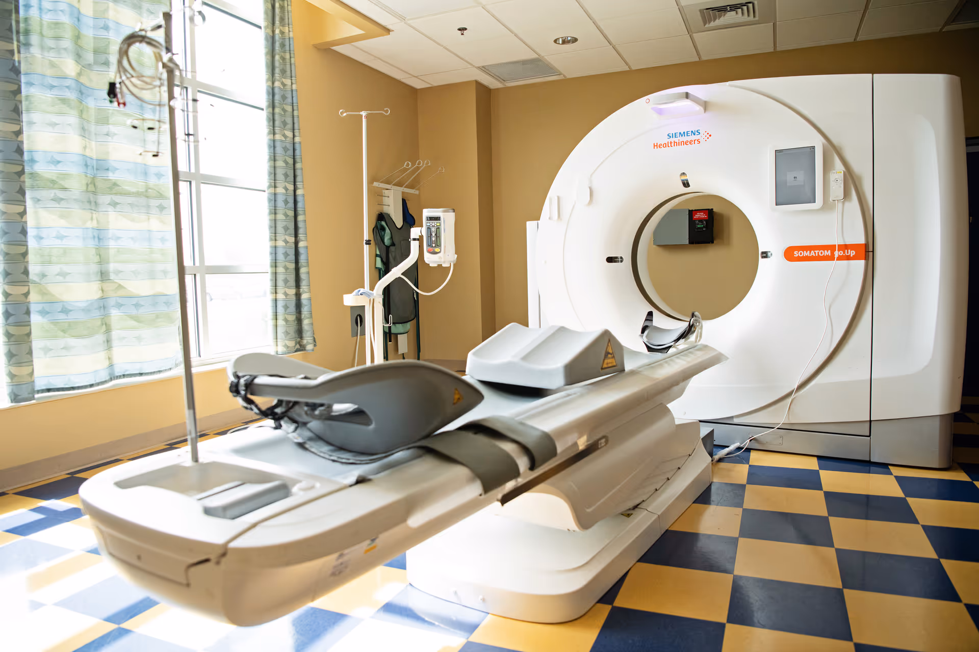 Hospital MRI suite featuring a large white MRI machine and patient bed in a tiled room.