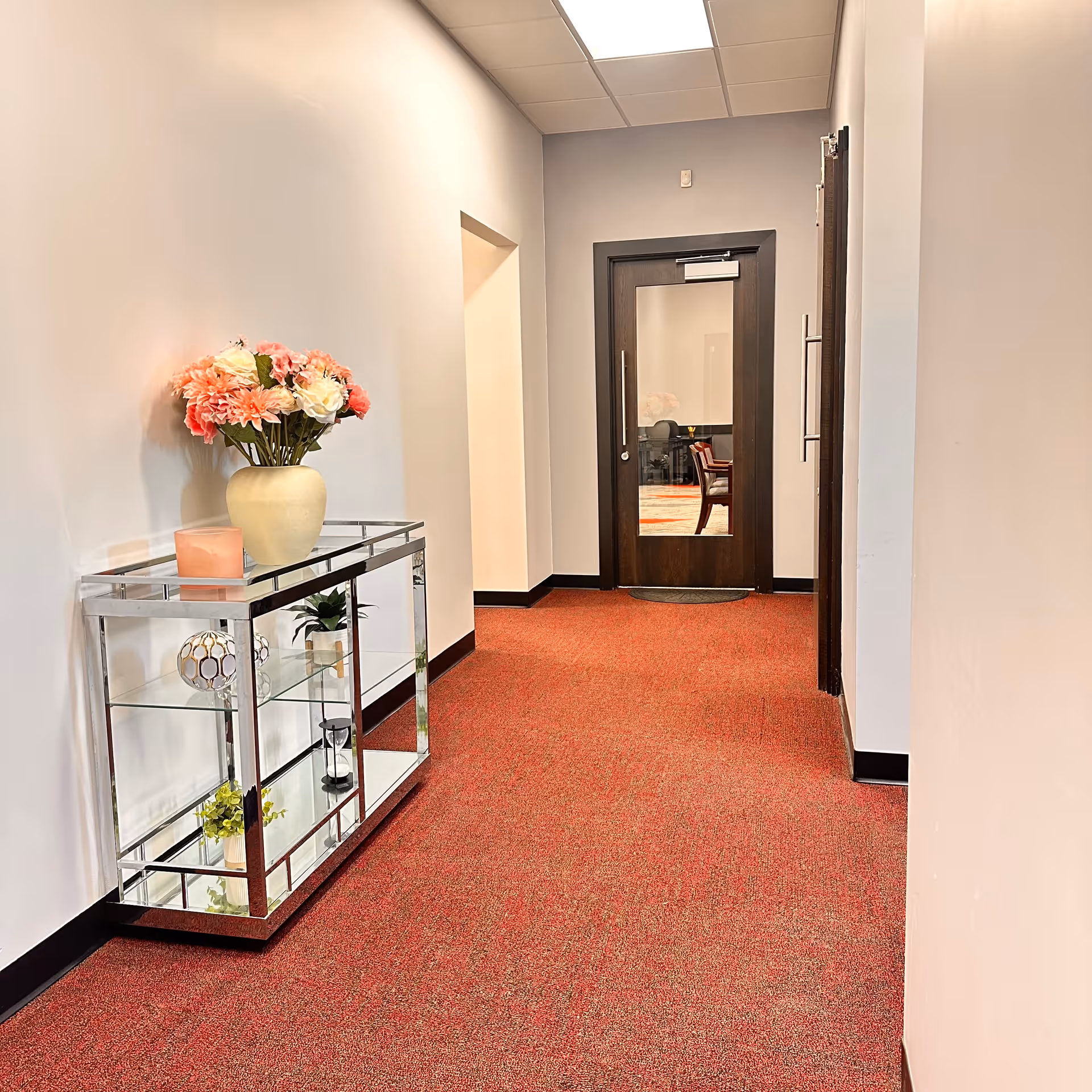 Hallway inside a senior living facility with a glass shelf and potted flowers.