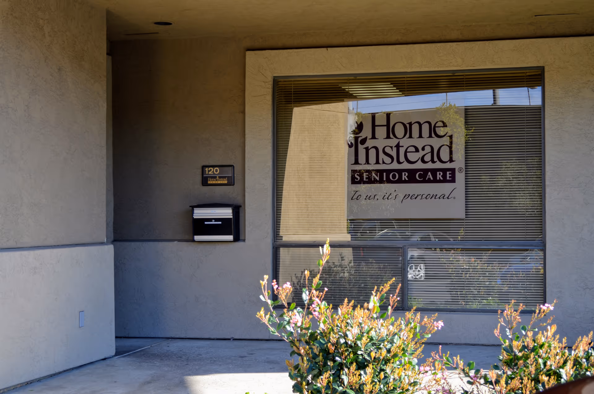 Exterior view of a beige building with Home Instead Senior Care sign in the window.