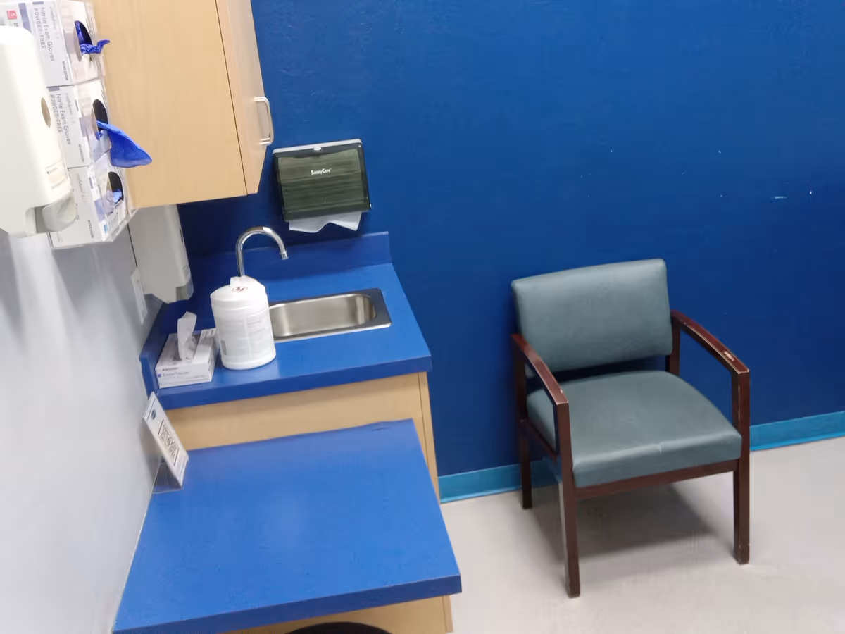 Blue kitchenette with sink, countertop, cabinets, and a chair against a blue wall.