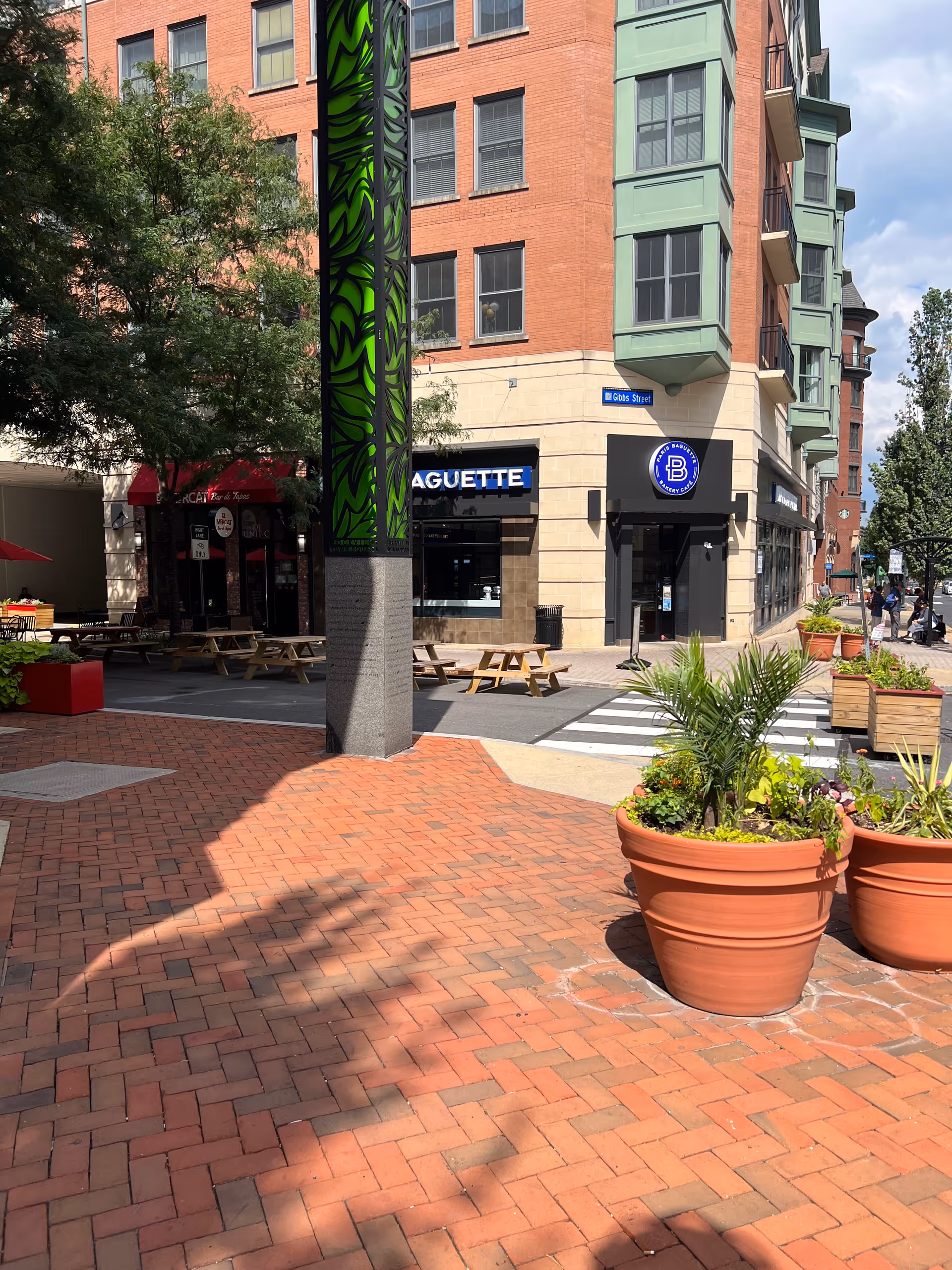 Outdoor urban plaza with brick pavement, planters, and storefronts