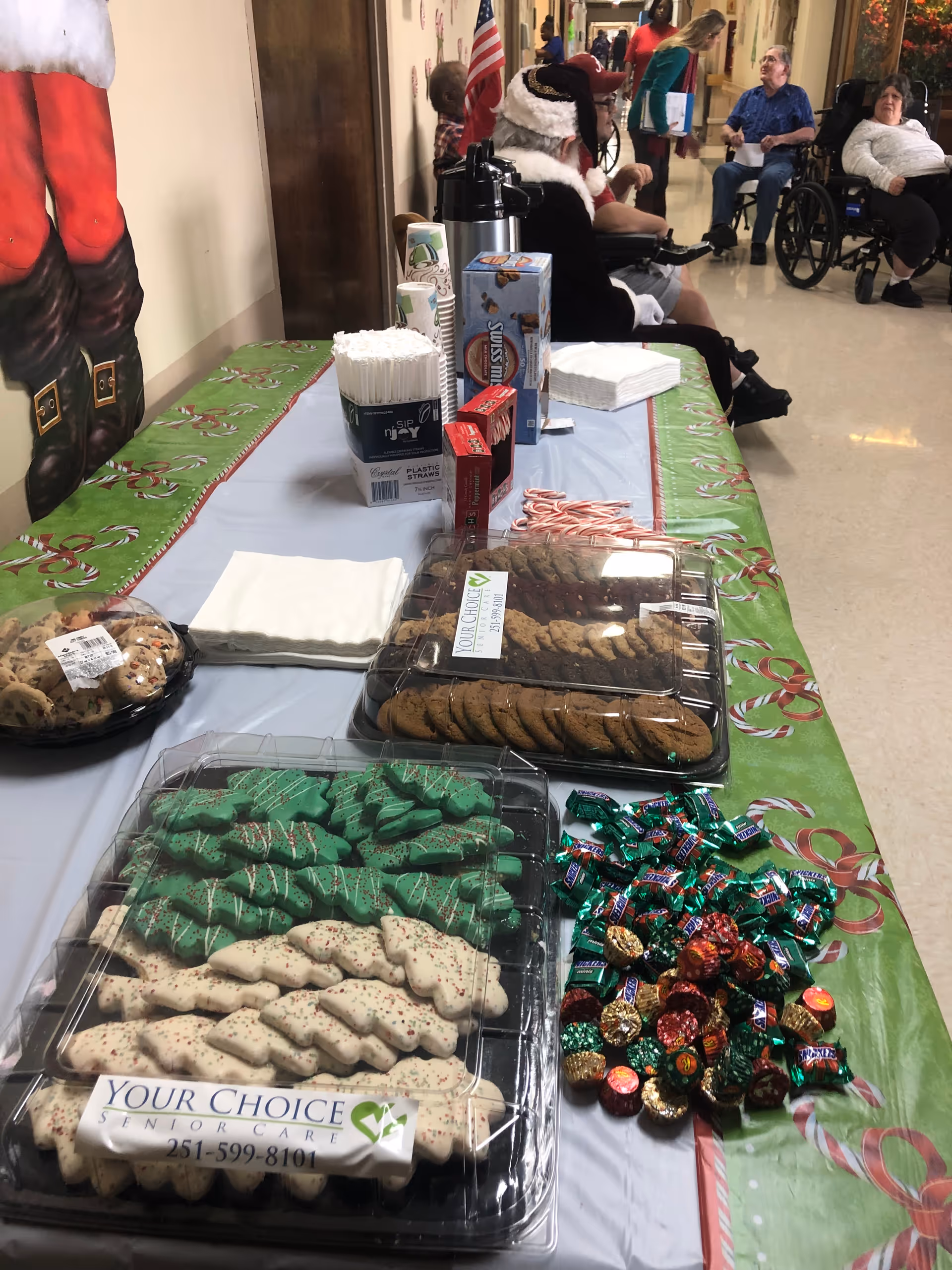Holiday snack table with cookies and candy in a senior care hallway, residents visible in background.