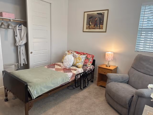 Cozy bedroom in a senior living facility with a bed, nightstand lamp, recliner, and closet.