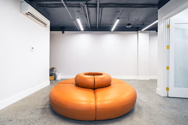 Modern lounge with a large orange circular couch in a white-walled room.