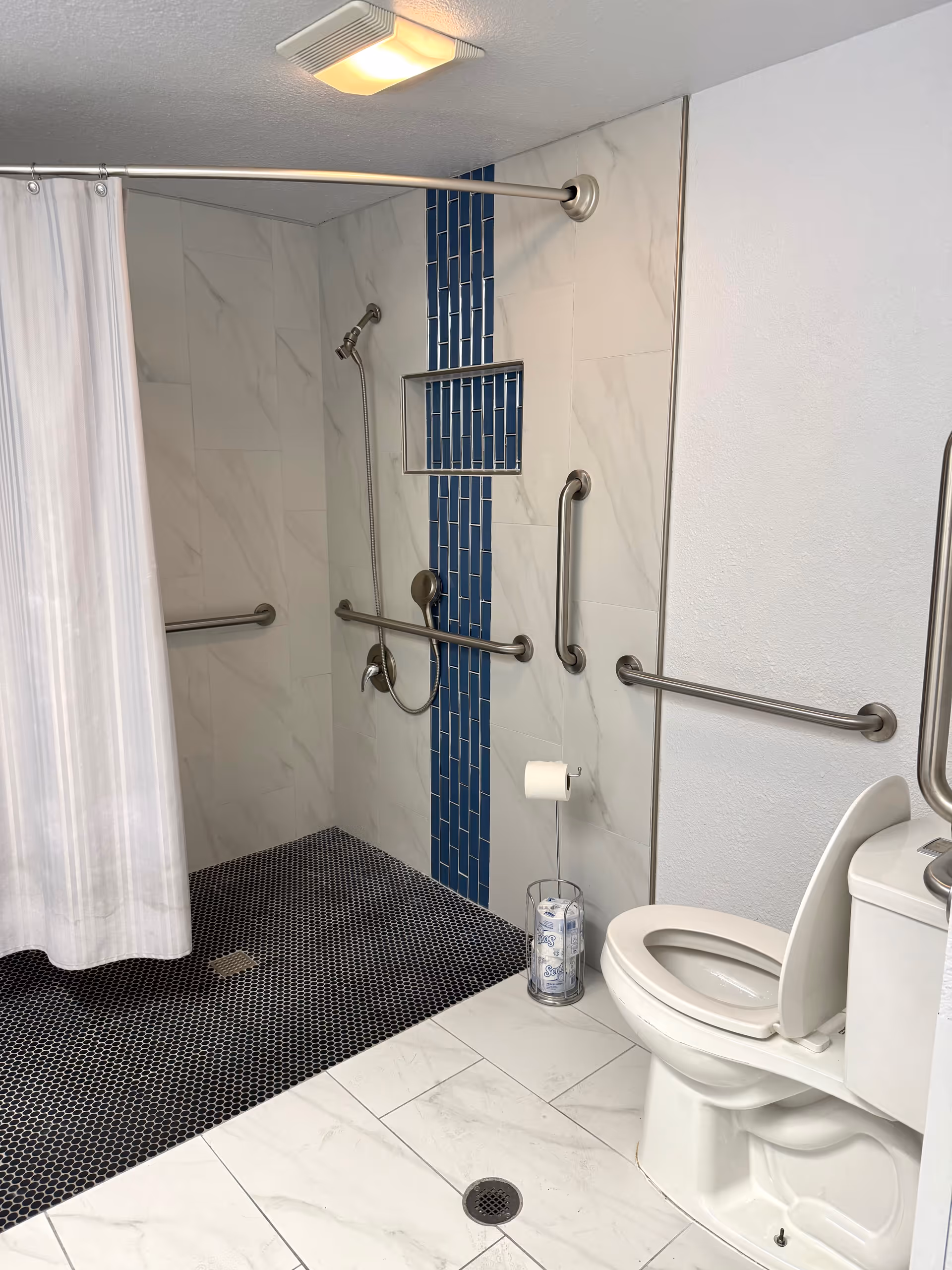 Accessible bathroom in a senior facility featuring a blue-tiled shower and multiple grab bars.