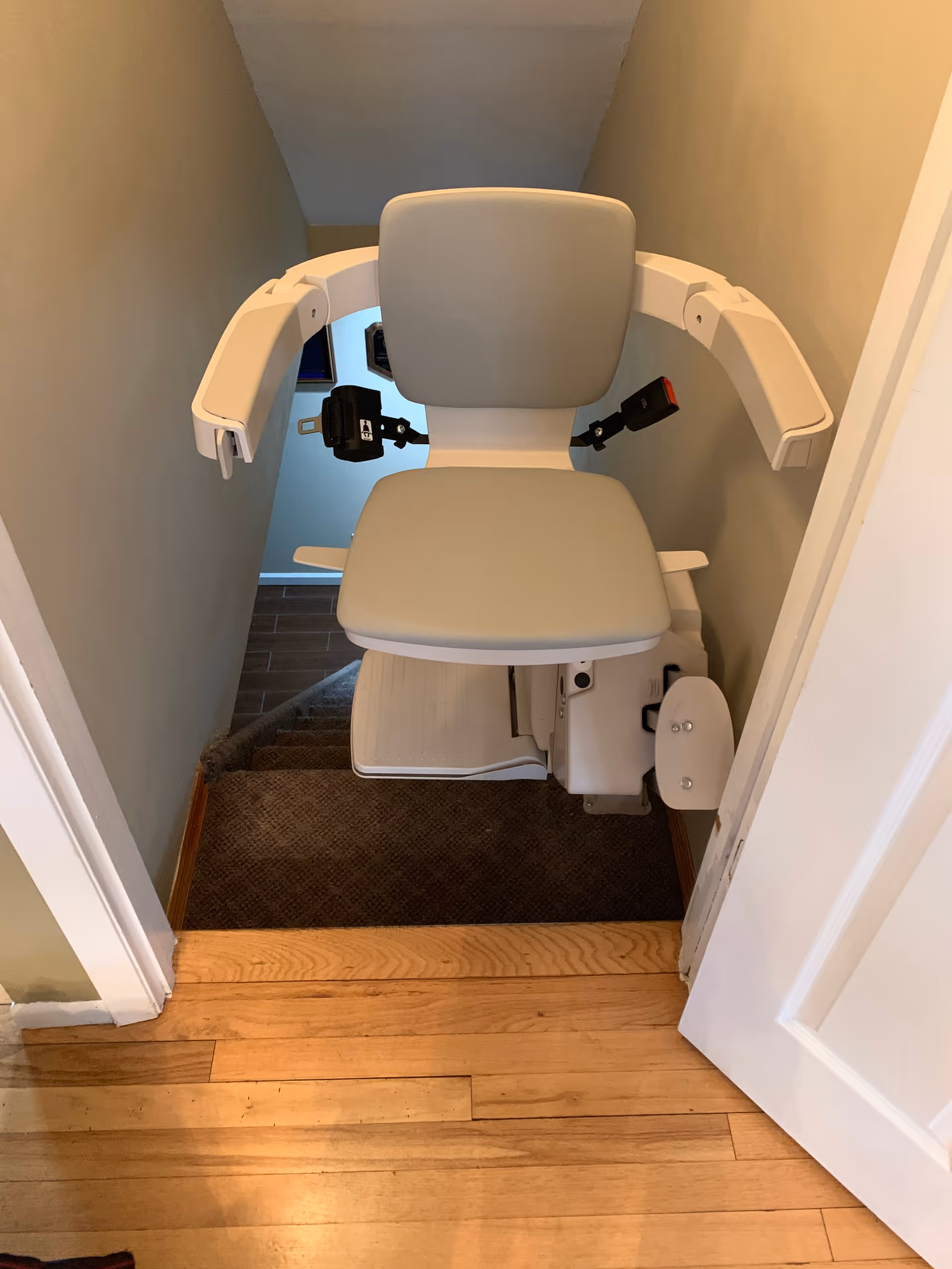 Gray stairlift chair mounted along a narrow staircase in a residential hallway.