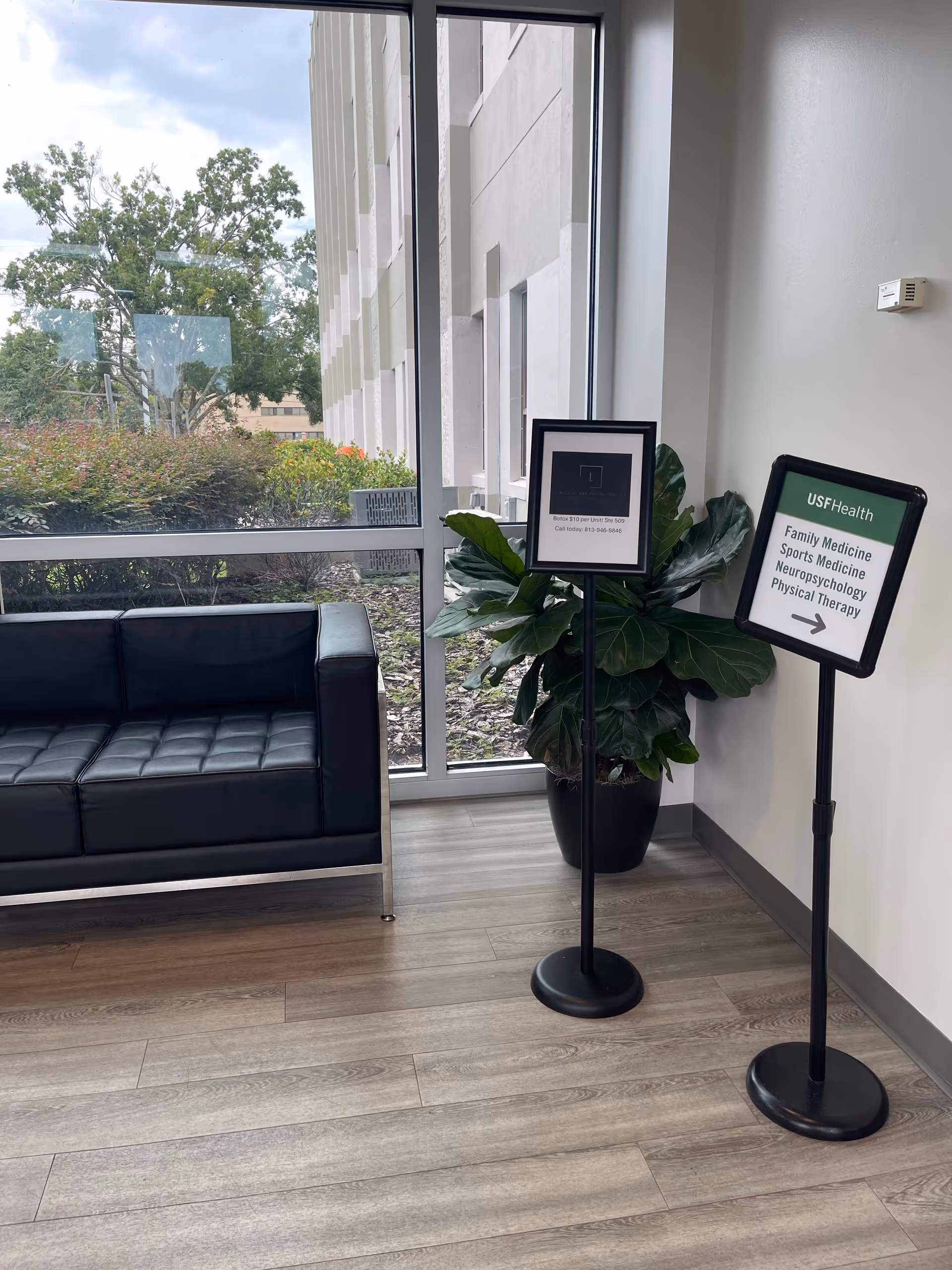 Modern interior lobby with a black leather couch, large windows, and signage on stands.