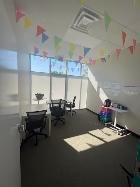Bright interior study room with desks, chairs, bunting, and large sunlit windows.