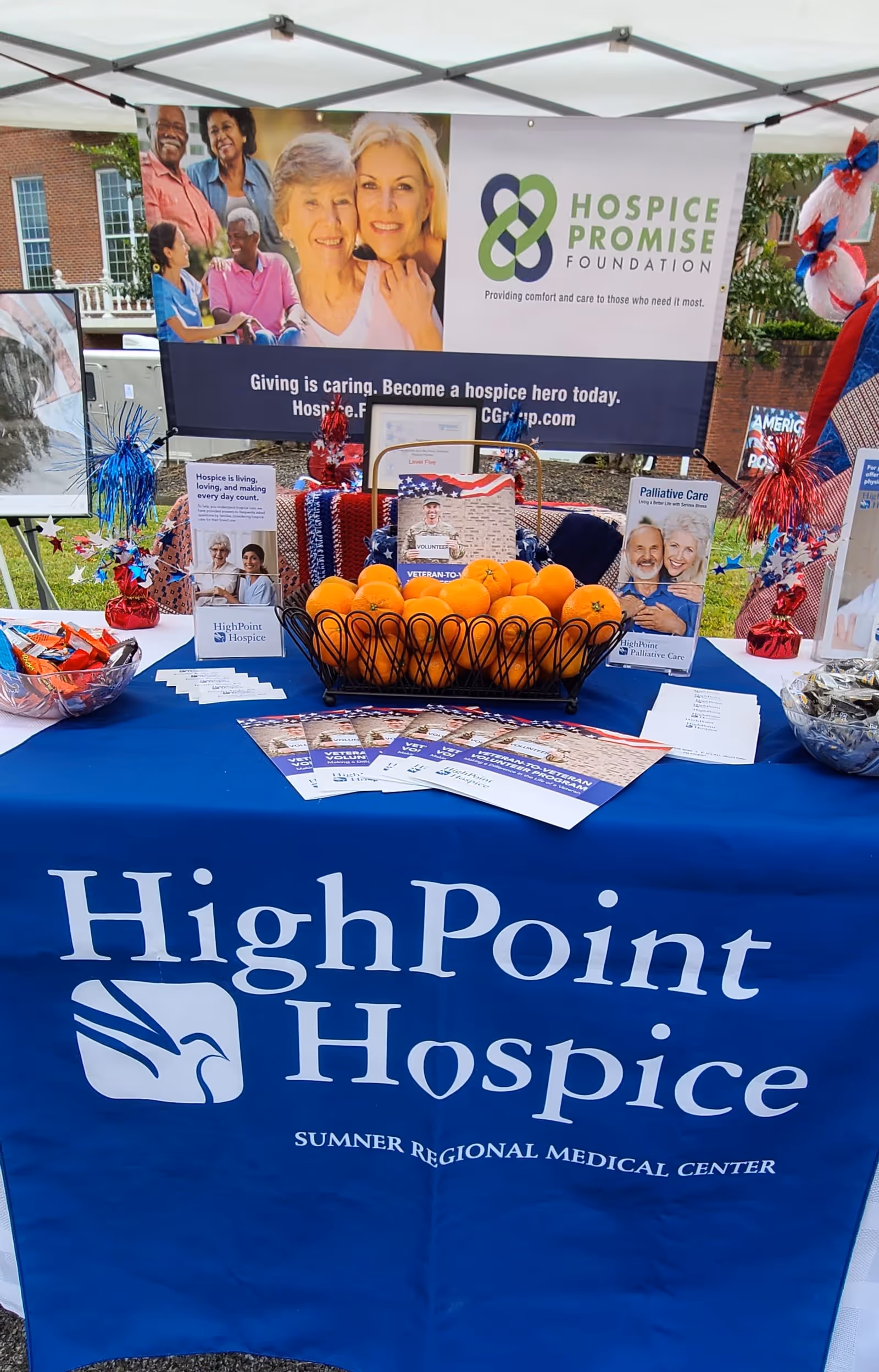 Outdoor promotional booth for HighPoint Hospice with banners, brochures, and a bowl of oranges.