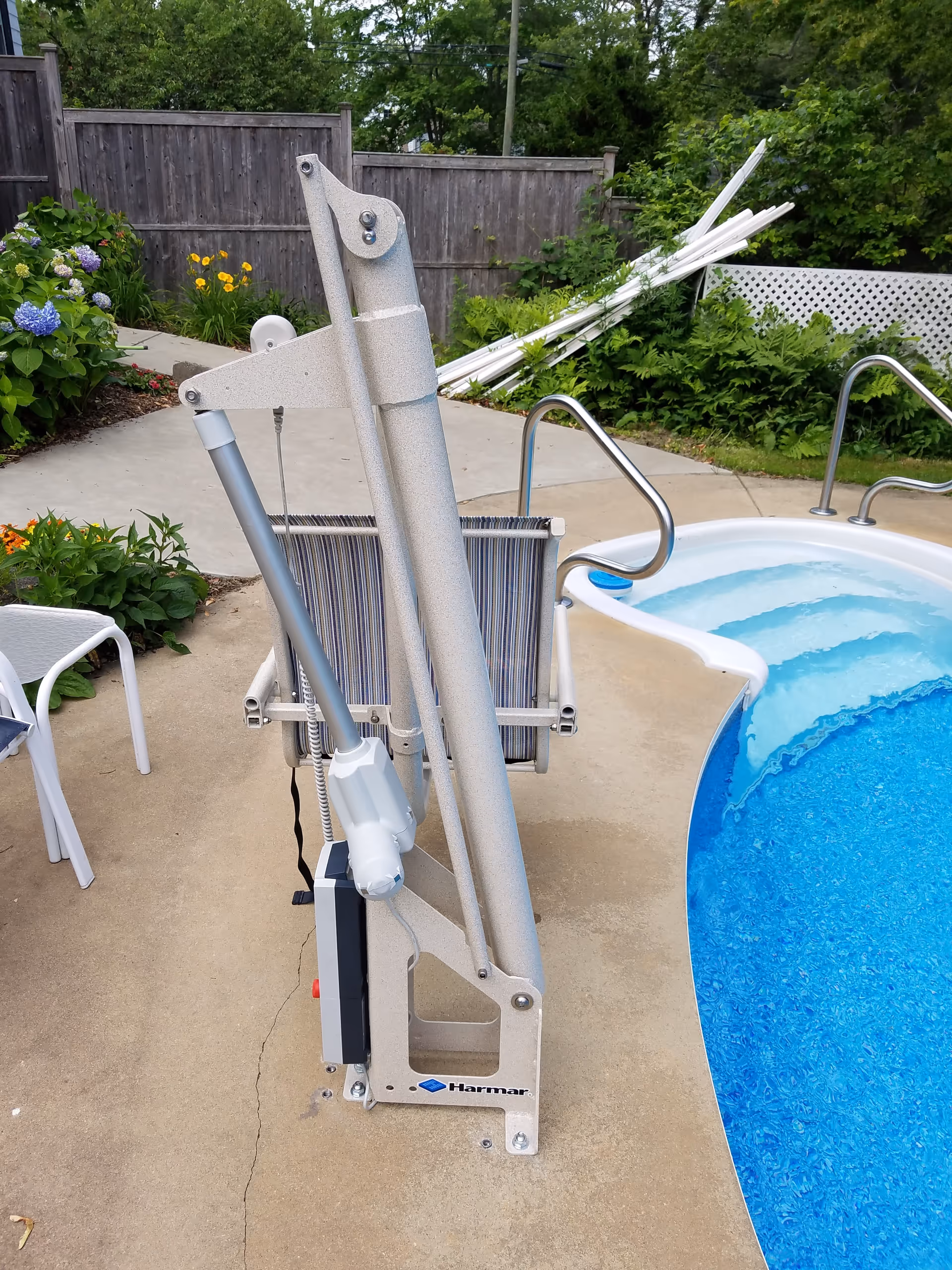 Poolside hydraulic lift device beside a blue pool in a fenced outdoor area.