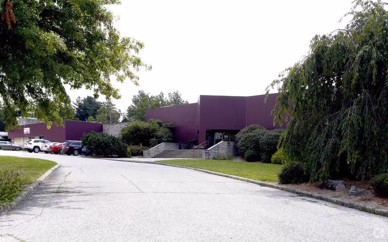 Front view of a purple-surfaced senior care facility with driveway, parked cars, and greenery.
