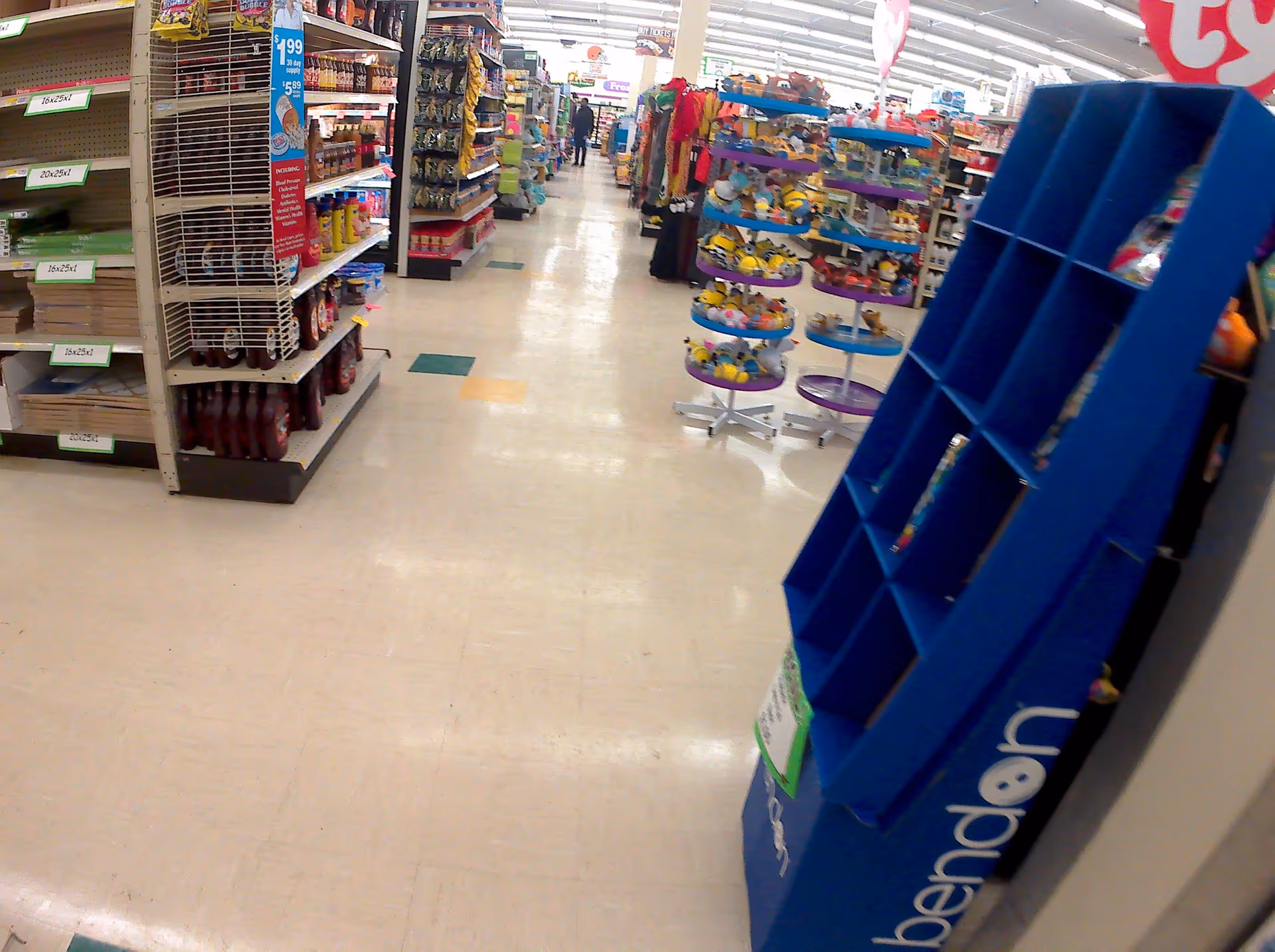 Aisle view inside a drugstore with shelves, displays, and blurred shoppers.