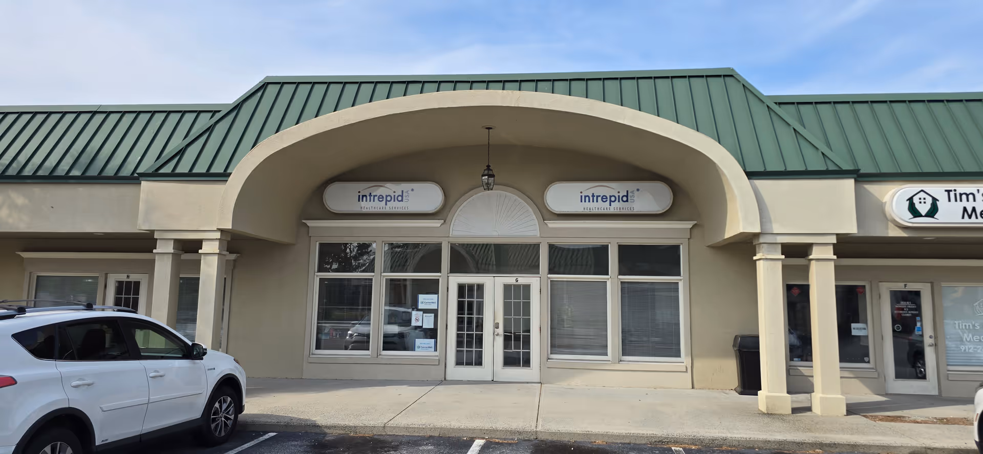 Exterior storefront with arched entrance and signs, parked car in front.