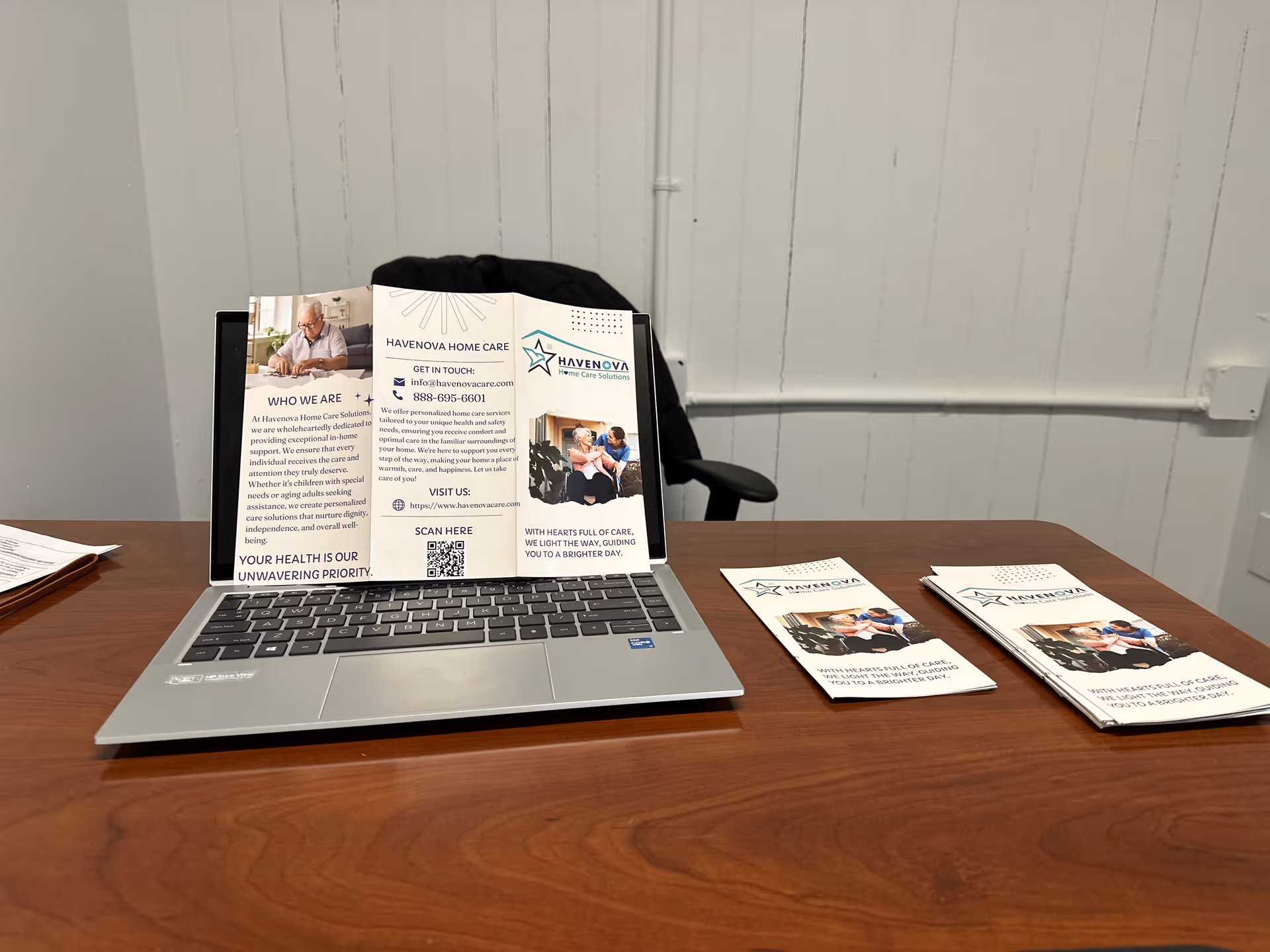 Laptop on wooden desk with Havenova Home Care Solutions brochures spread nearby.
