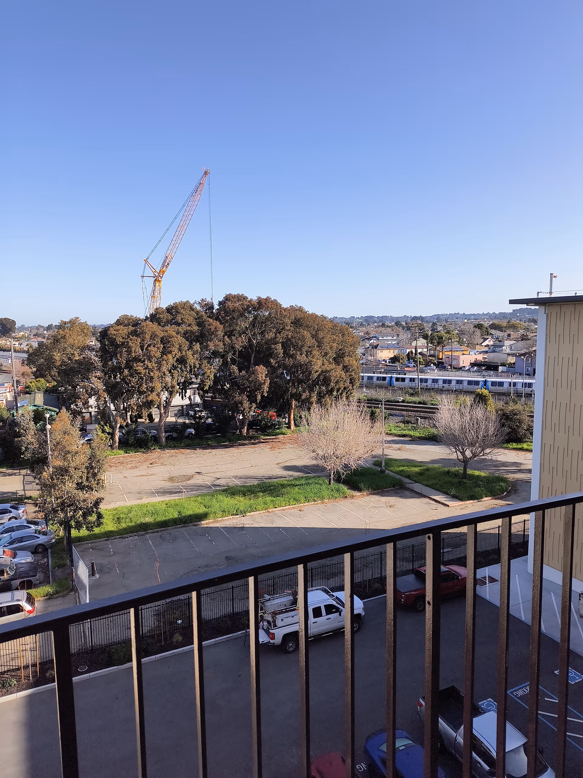 Balcony view overlooking parking lot, trees, and a distant construction crane.