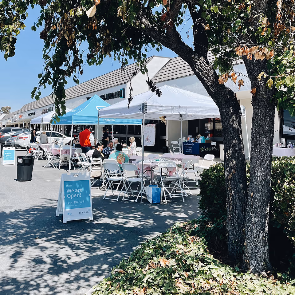Outdoor event in a parking lot with tents, tables, chairs, and people outside Titanium Healthcare.