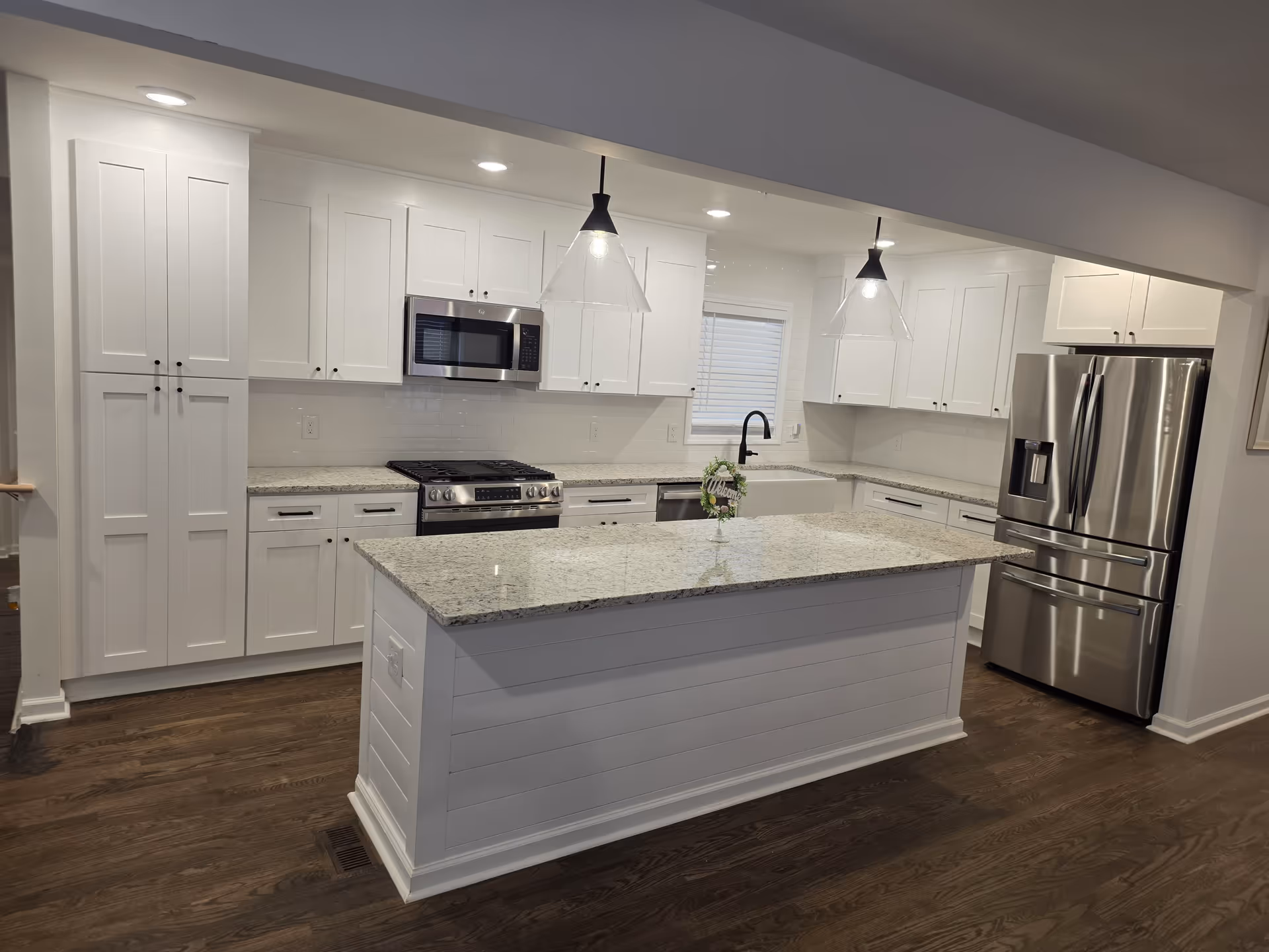 Bright white kitchen with island, granite countertops, stainless steel appliances, and dark hardwood floors.