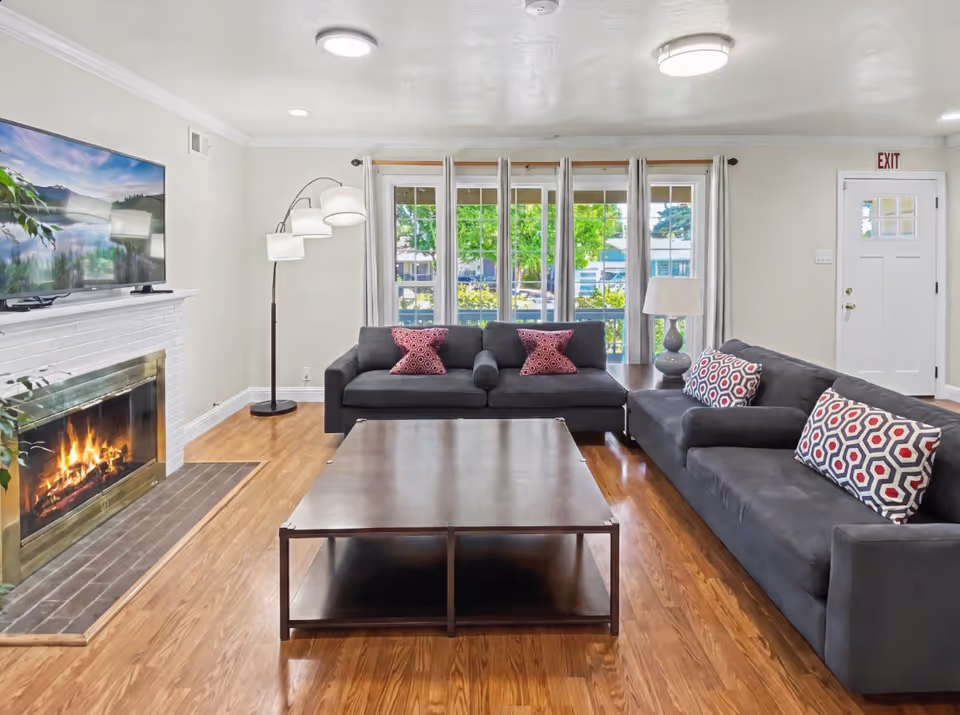 Cozy living room with gray sofas, coffee table, a fireplace, and large windows.