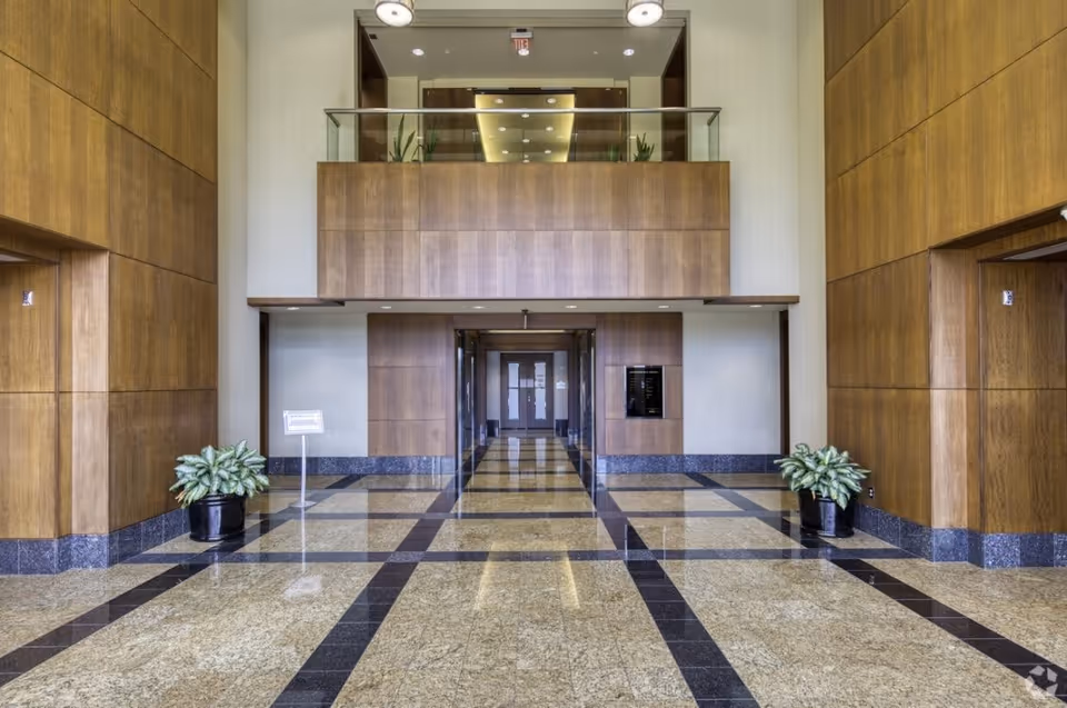 Bright interior lobby with wood panel walls, marble floor, and glass second-floor balcony.