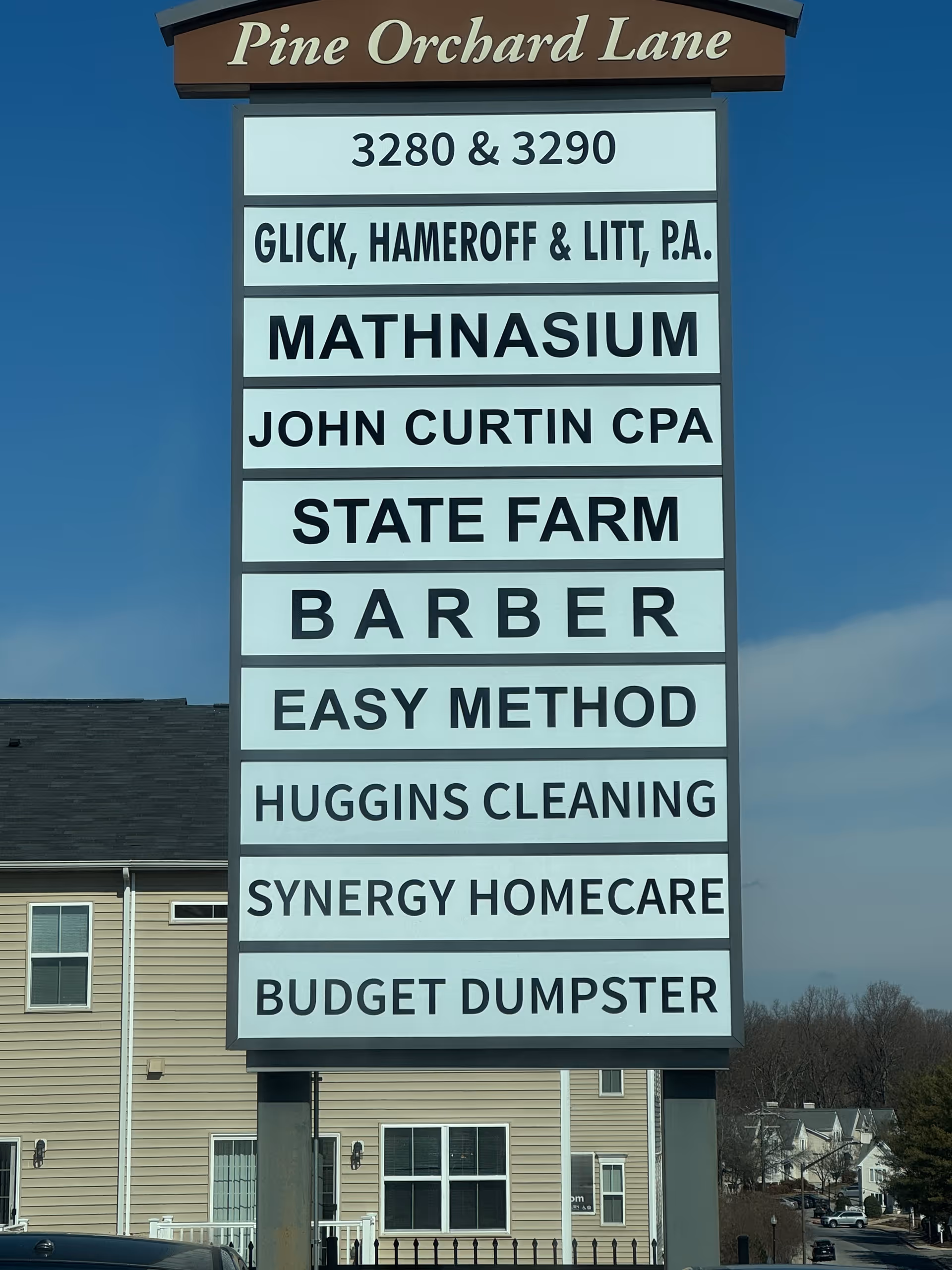 Tall outdoor signboard listing businesses, including SYNERGY HOMECARE, beside a beige storefront.