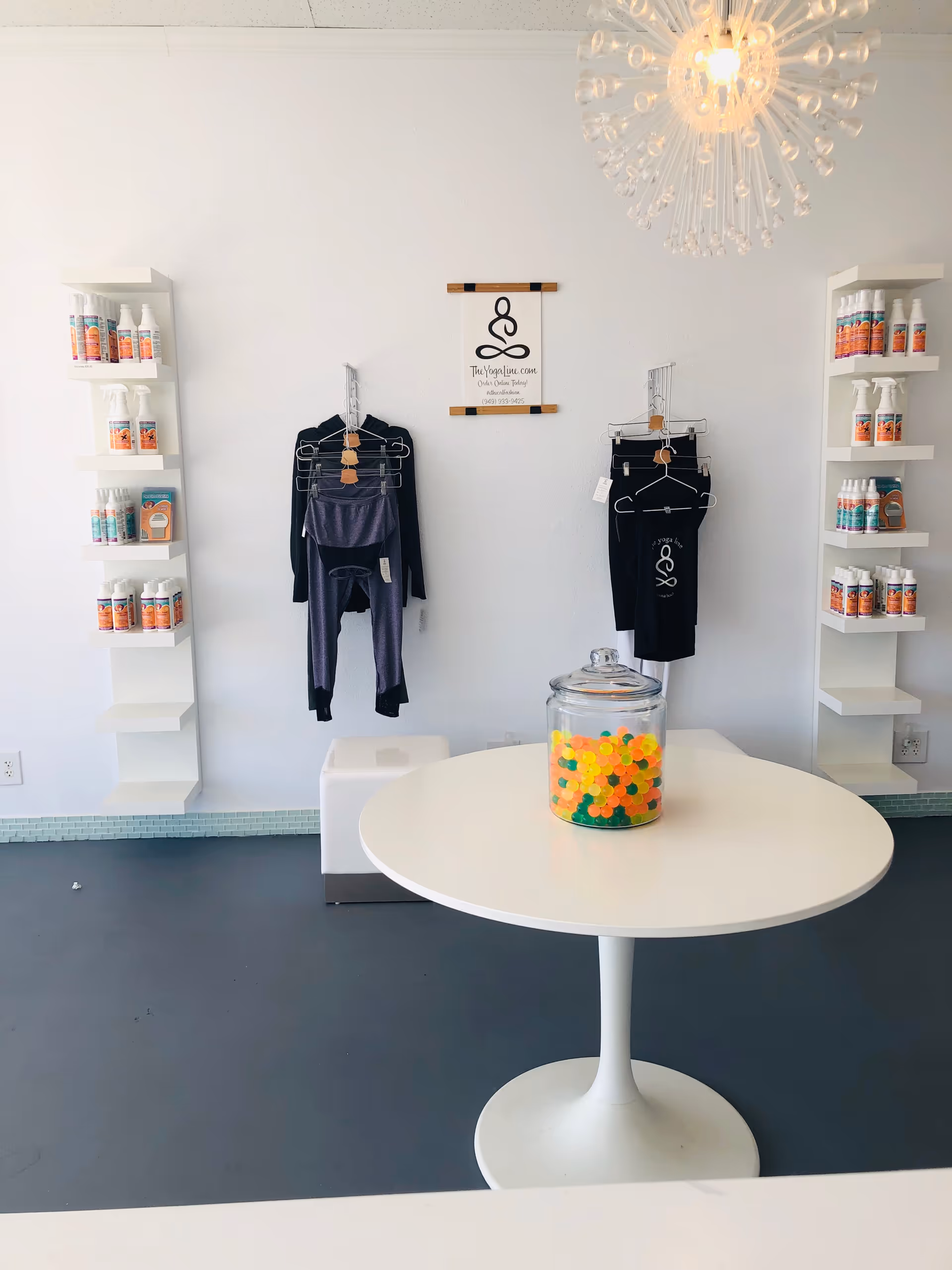 Bright interior with product shelves, hanging clothes, and a white round table holding a candy jar.