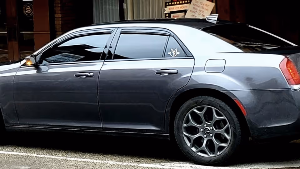 Blue-gray sedan parked on a city street beside a storefront.