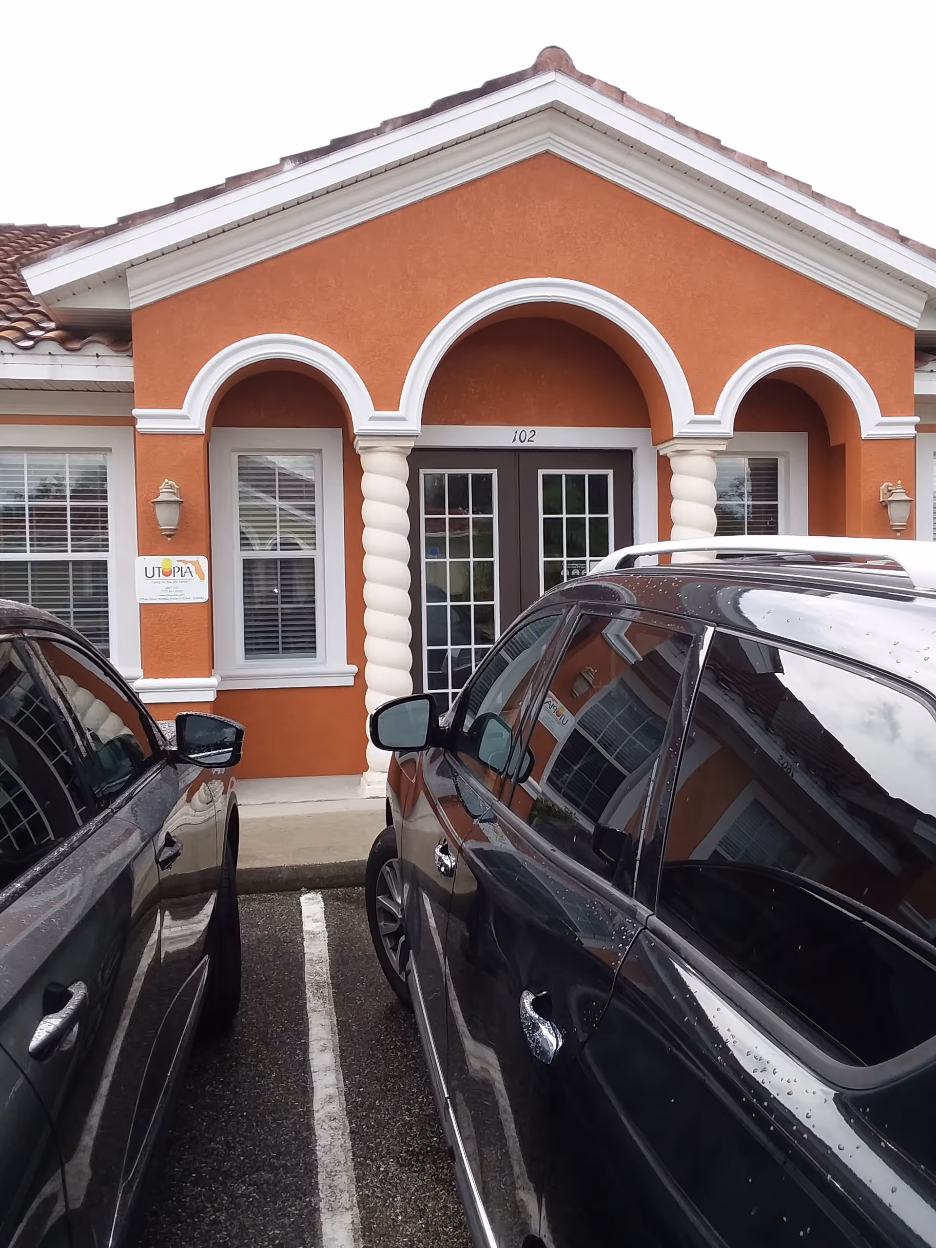 Orange Utopia Home Care, Inc. building entrance with arched white columns and parked cars.