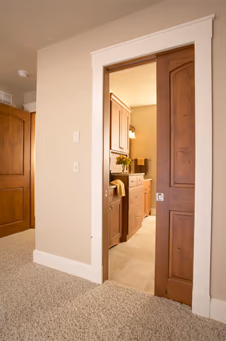 Open doorway reveals a bathroom with dark wood cabinets and beige walls.