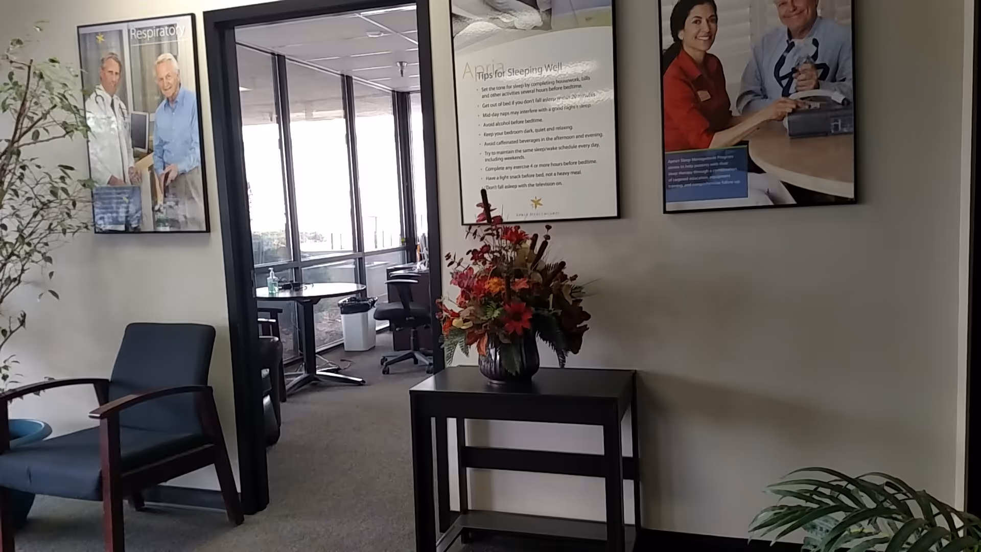 Interior lobby of a senior facility with blue chairs, flowers, and wall posters.