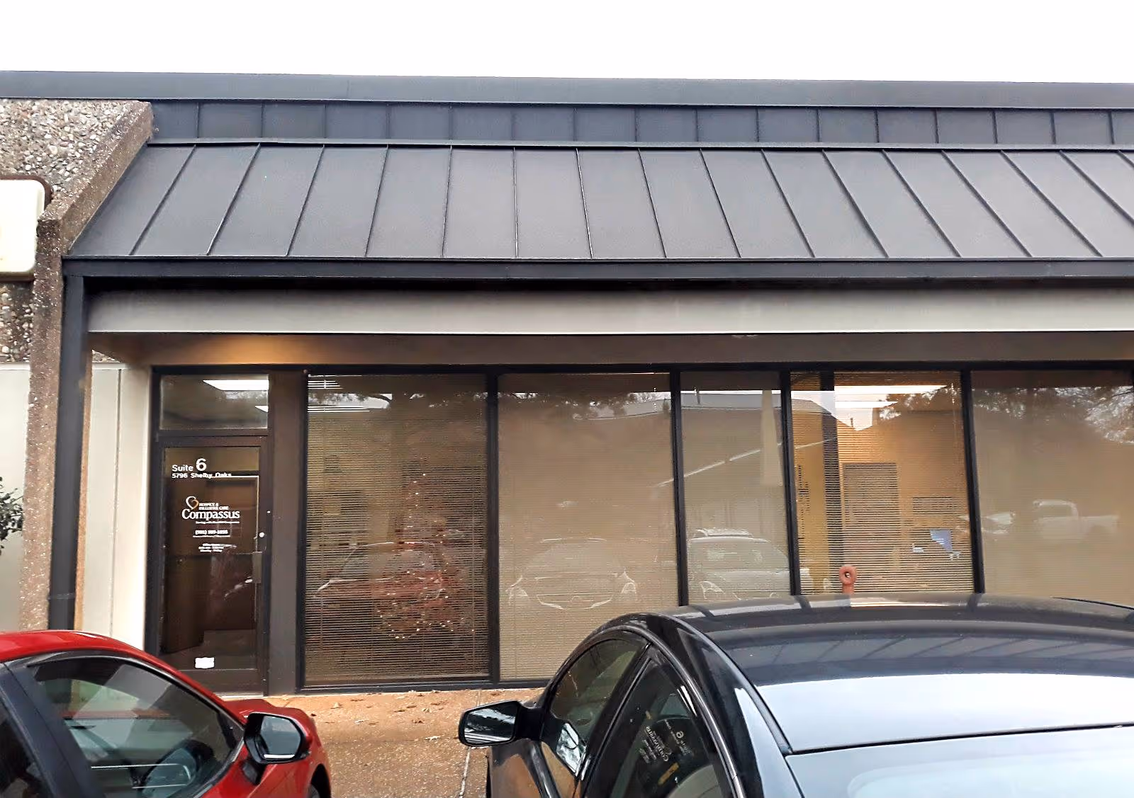 Exterior view of a Compassus facility with glass storefront, entrance door, and parked cars.