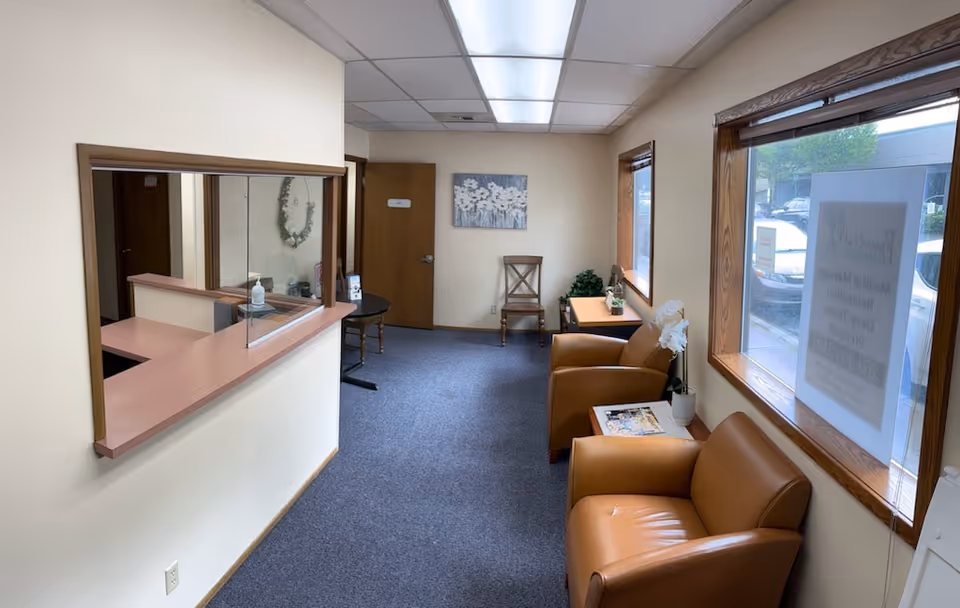 Reception area with brown leather chairs, windows, and a service counter inside a care facility.