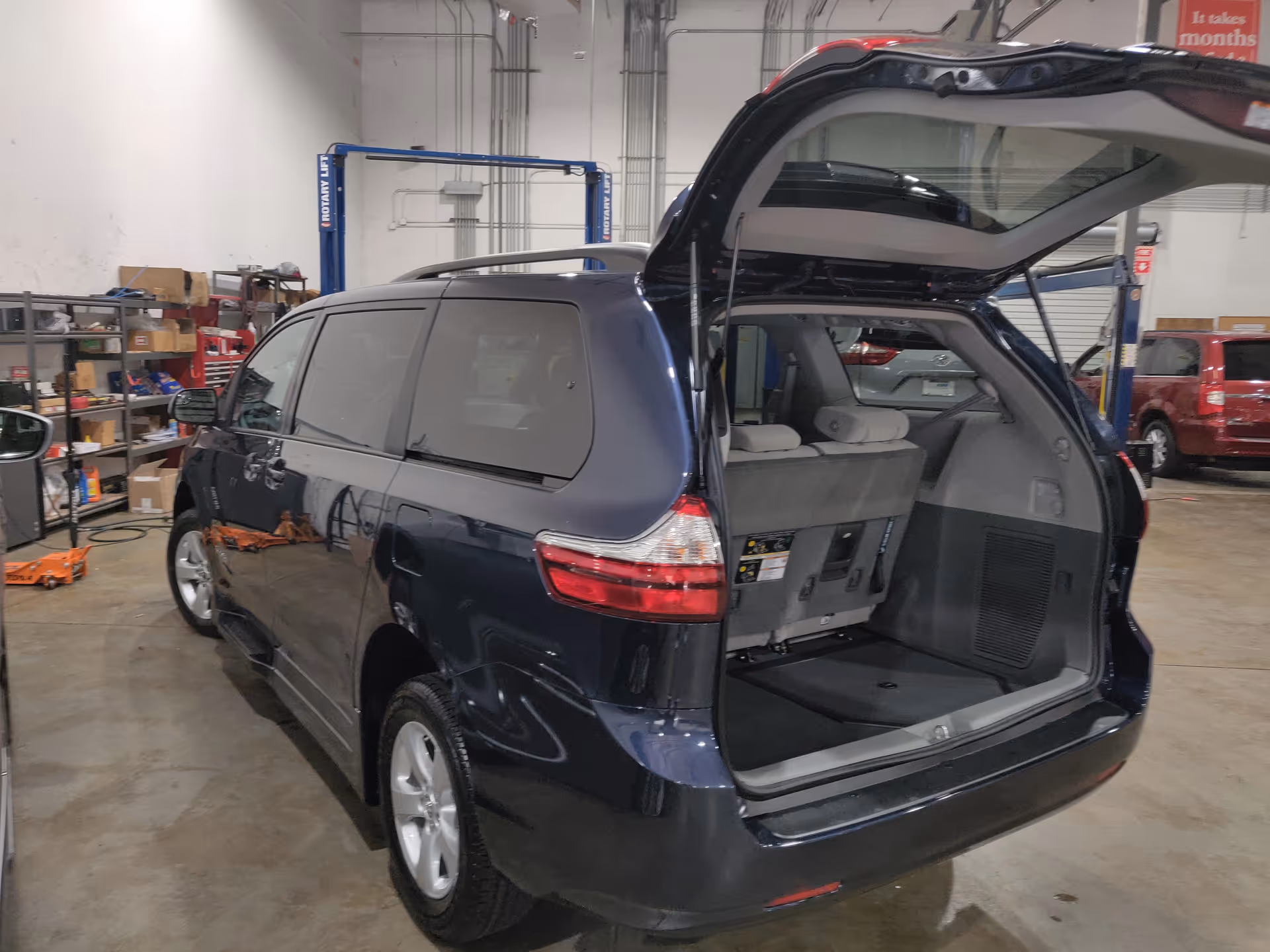 Blue minivan with open rear hatch inside a vehicle service workshop