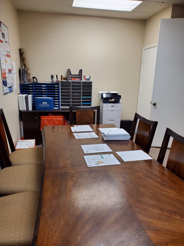 A long wooden conference table with papers sits in a beige office room.
