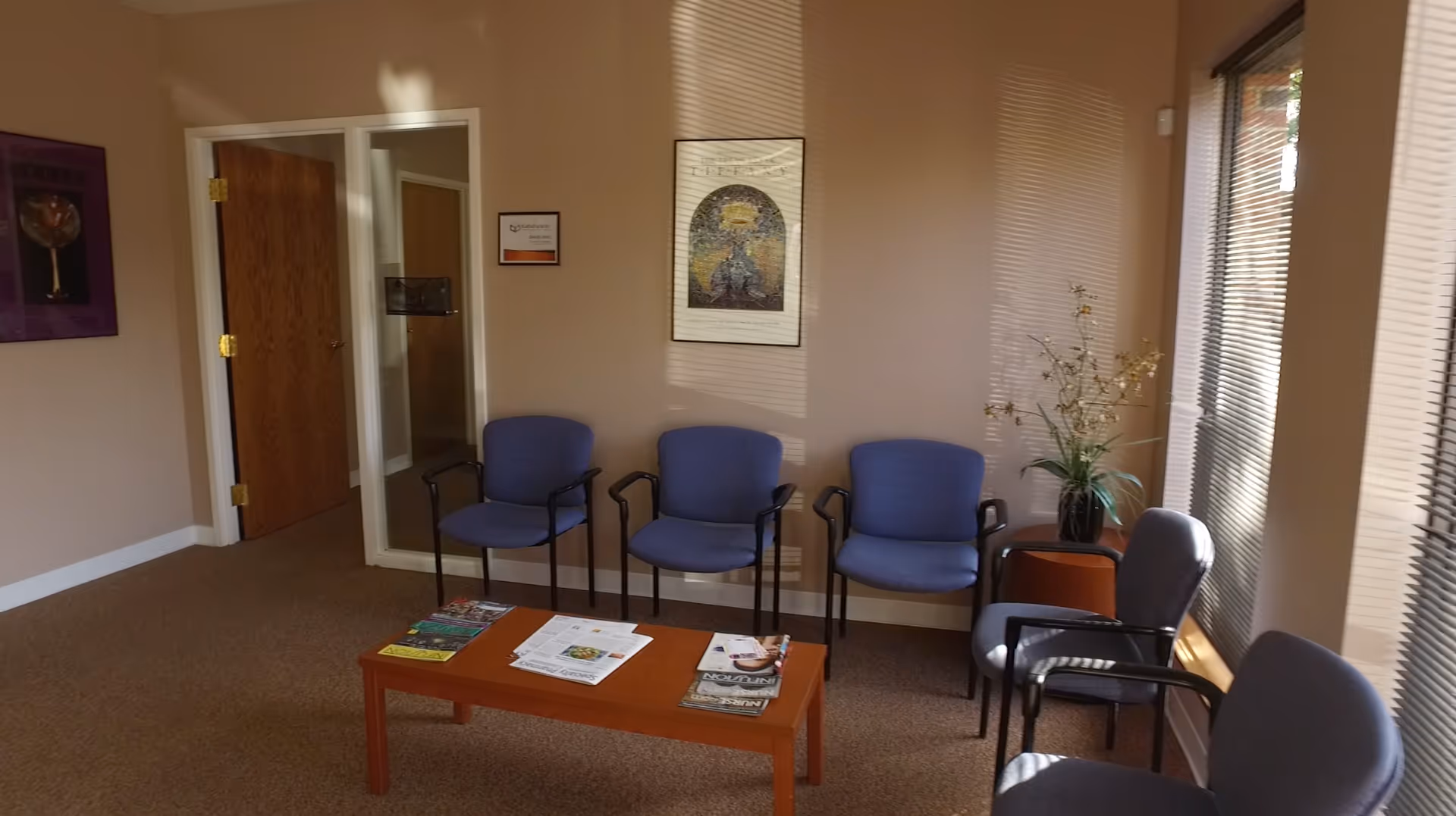 A waiting room in a senior facility with blue chairs and magazines.