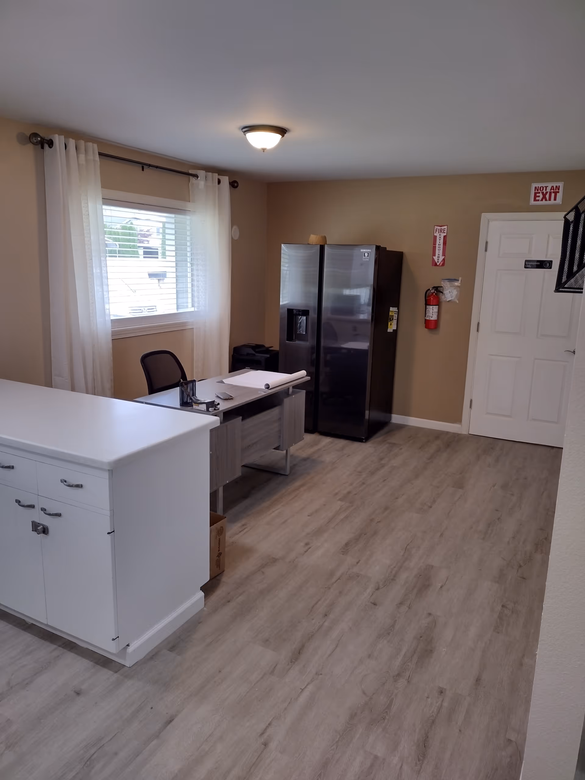 Bright, modern kitchen area with a desk, white cabinets, and a stainless steel fridge.