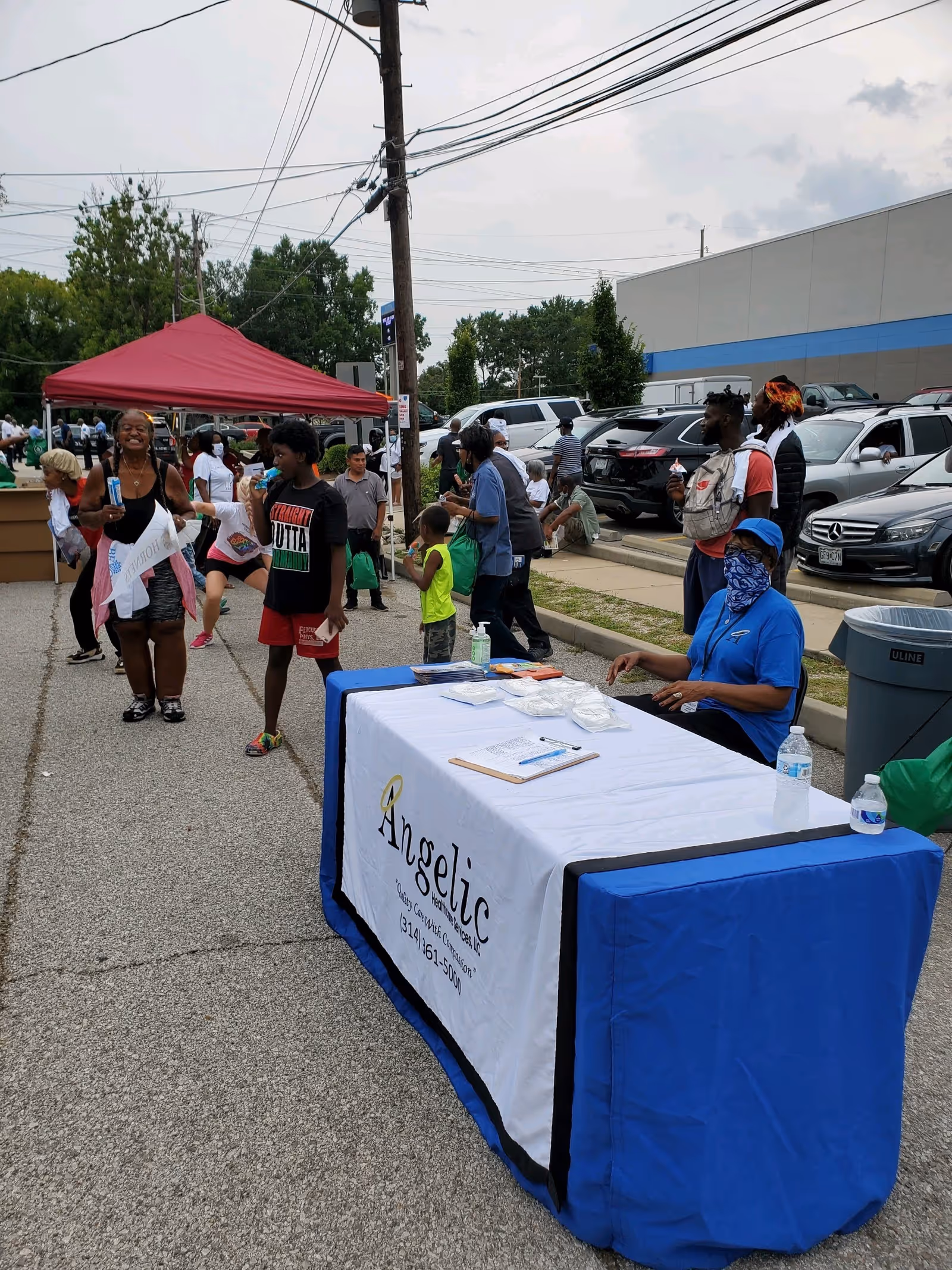 Outdoor community event with Angelic Healthcare Services LLC table and attendees.