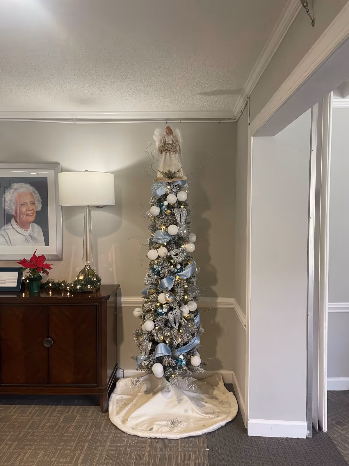 Decorated holiday tree in a hallway beside a wooden console and framed portrait.