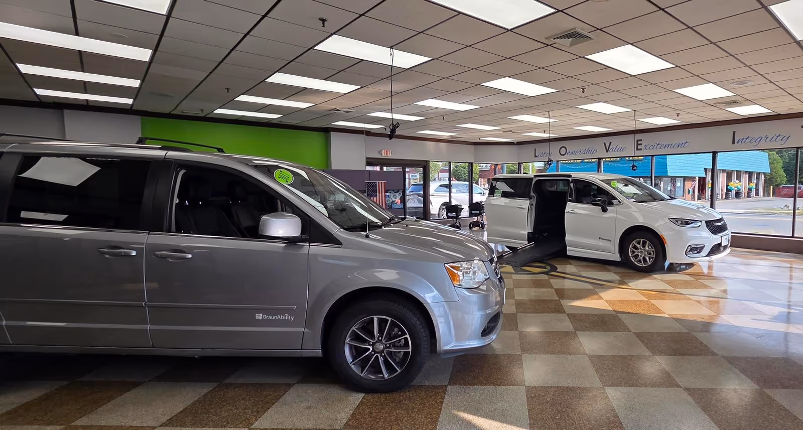Two minivans are displayed inside a MobilityWorks showroom with checkered tile flooring.