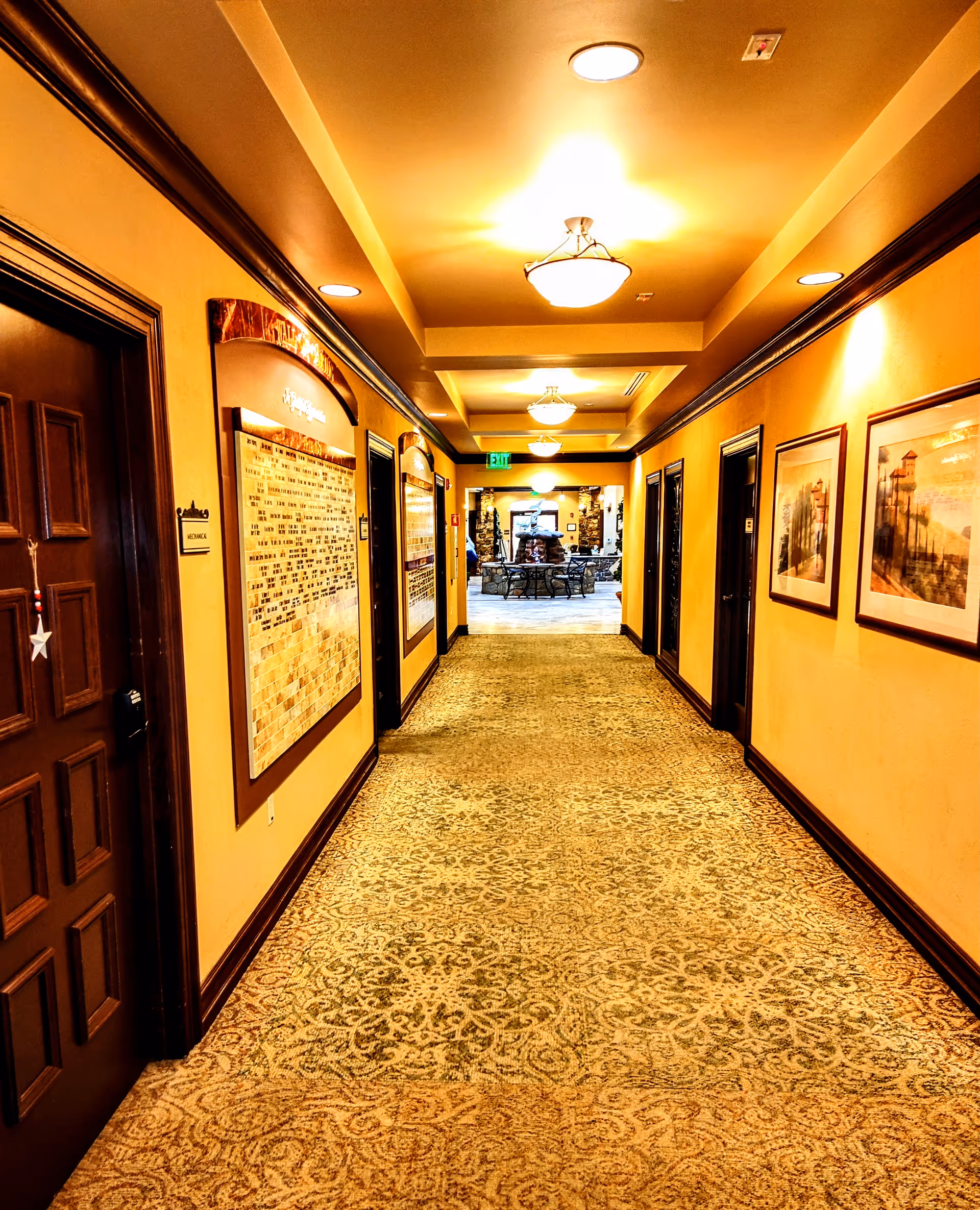 Warm, well-lit interior hallway of a senior living facility with wall art and carpet.