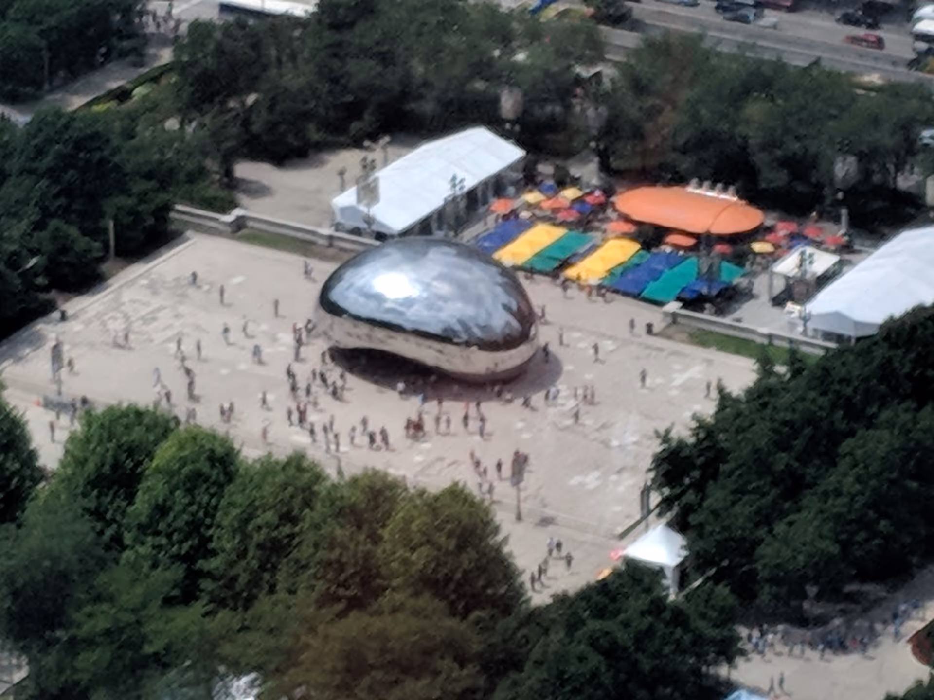 Aerial view of a reflective dome sculpture in a plaza with colorful tents and people