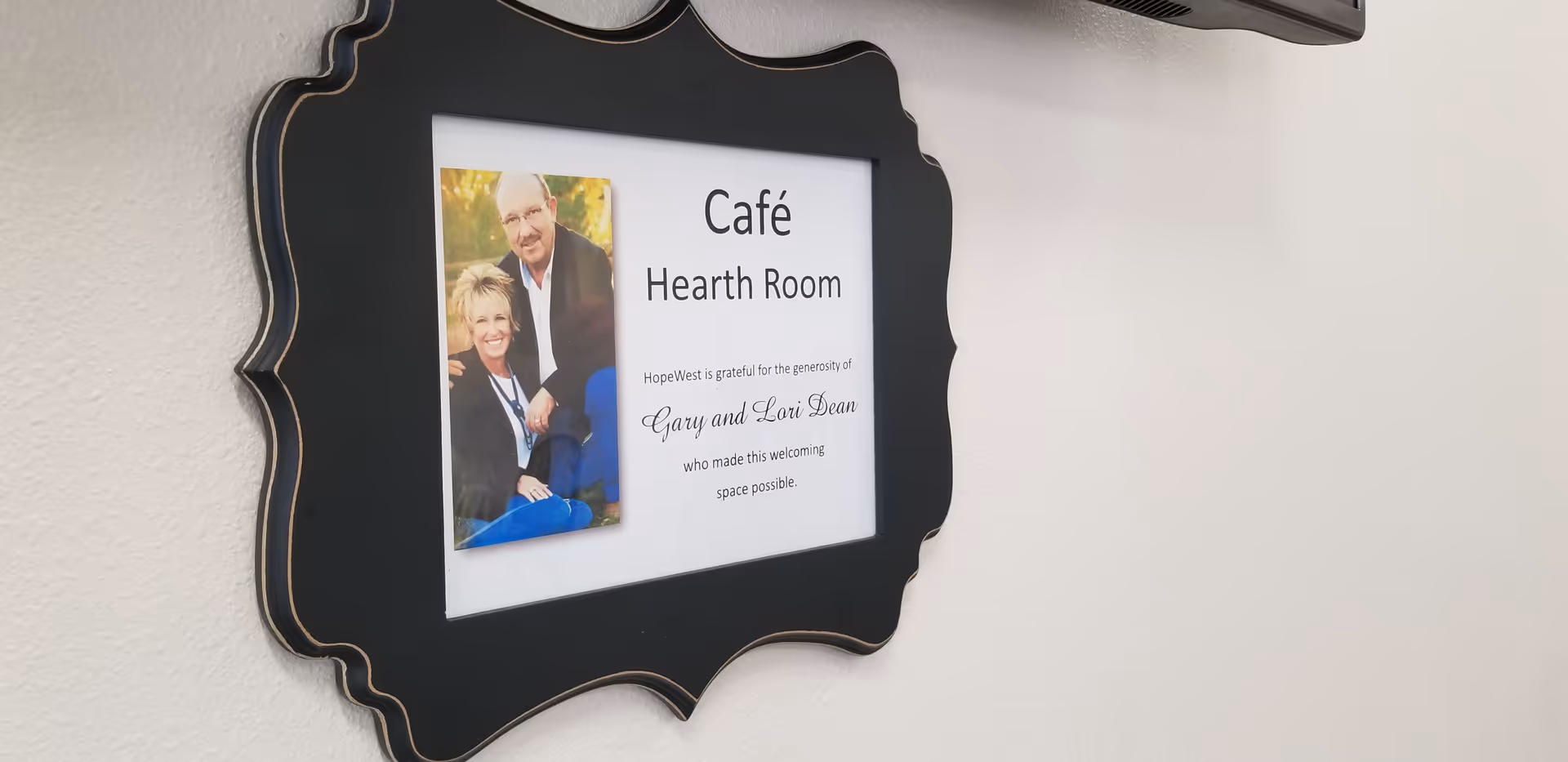 Ornate framed sign on wall reading Café Hearth Room with photo.