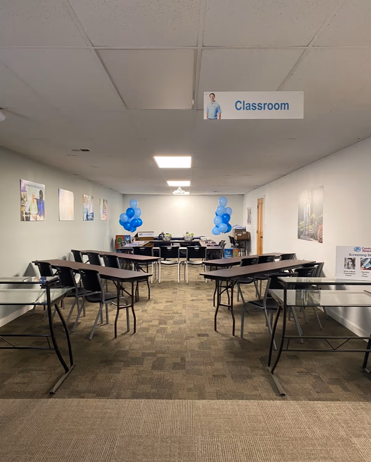 Long classroom-style room with desks arranged in rows, blue balloons, posters, and a hanging Classroom sign.