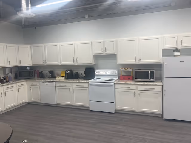 Long, bright kitchen with white cabinets, countertops, a stove, fridge, and small appliances.